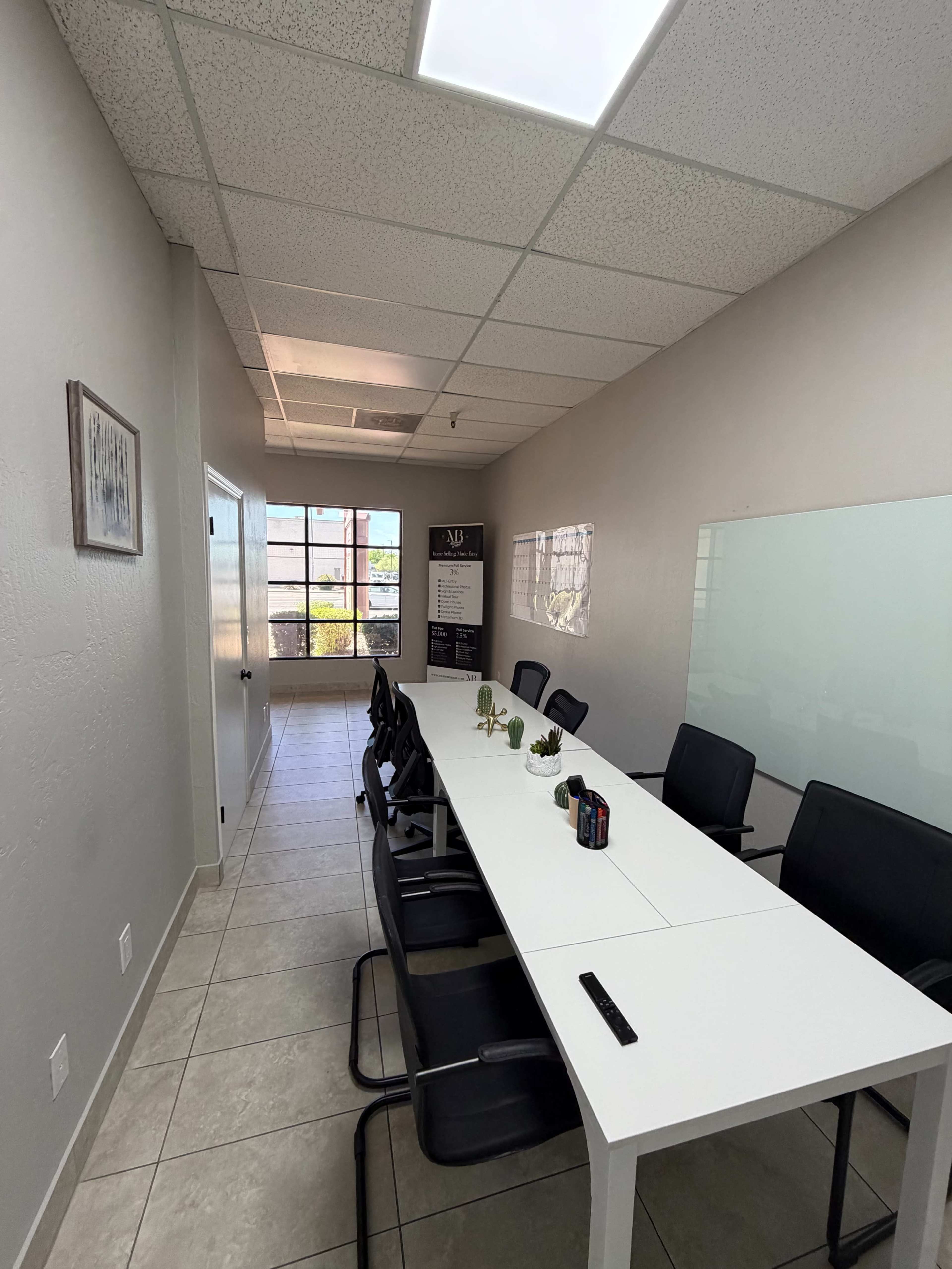 A clean, modern conference room features a long white table surrounded by black chairs and a large window letting in natural light.