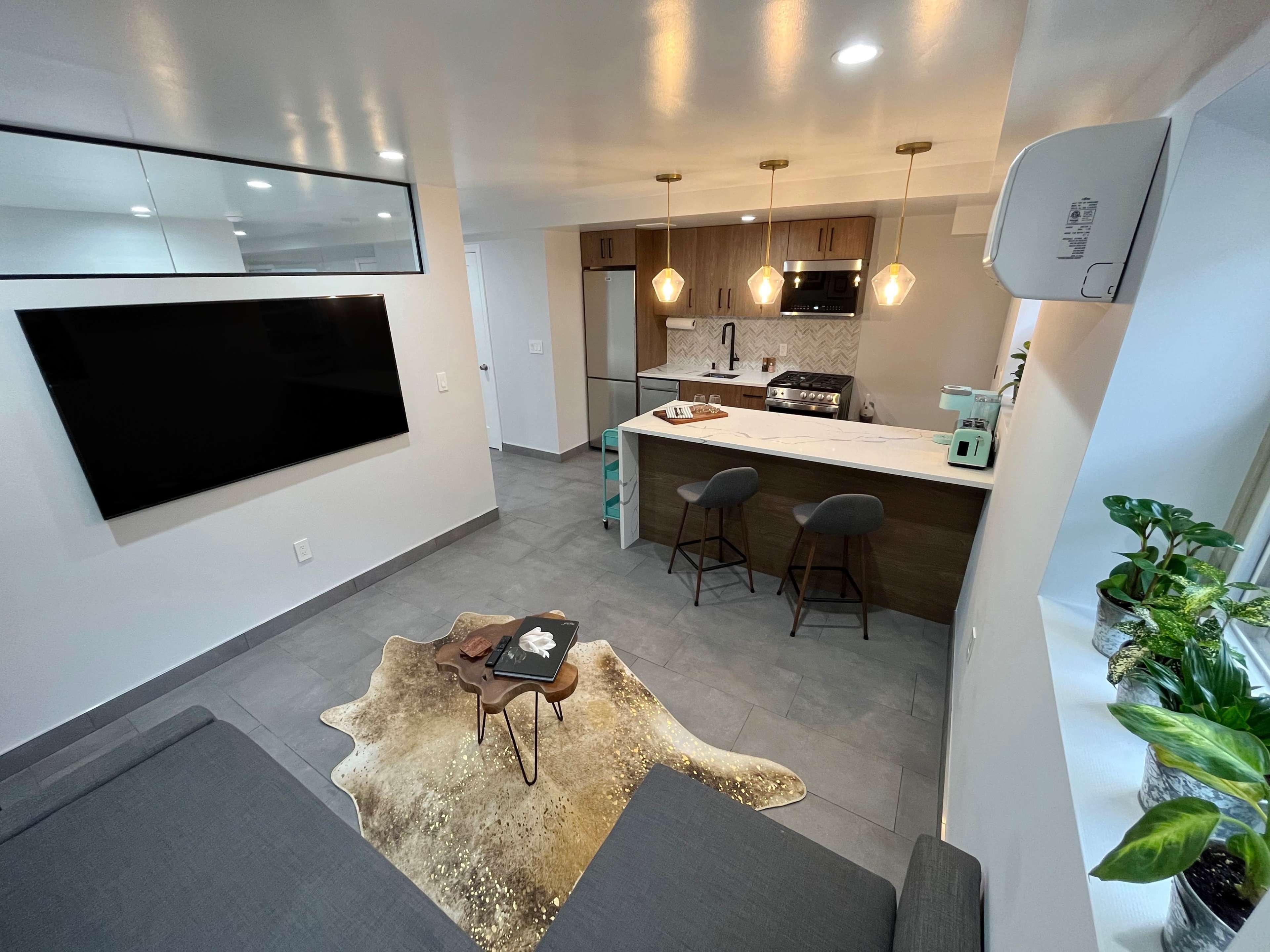 A modern living space with a kitchen area featuring bar stools, a television mounted on the wall, and a decorative rug on the floor.