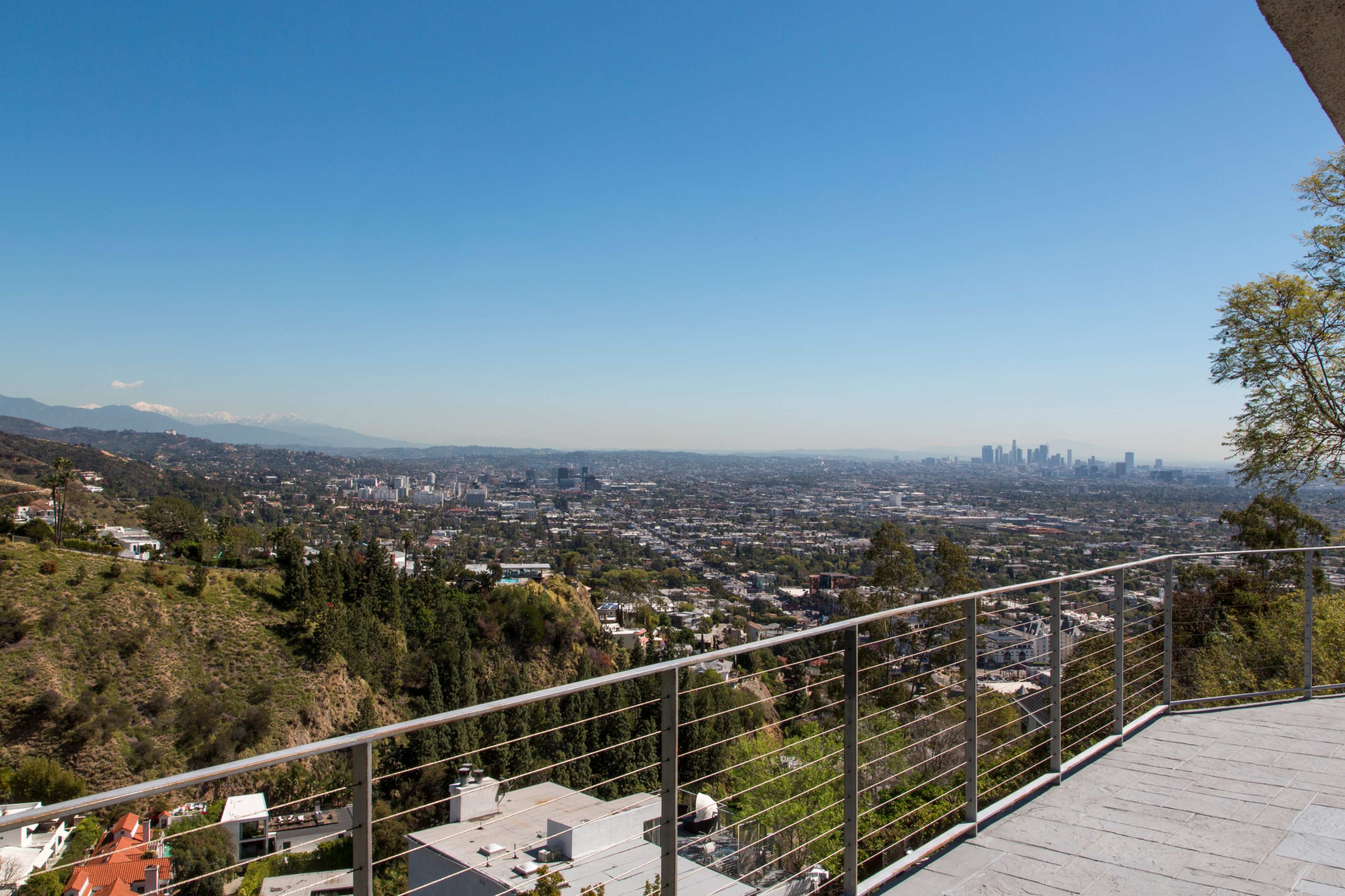 A panoramic view of a city skyline with a mountain range in the background, framed by a balcony railing.
