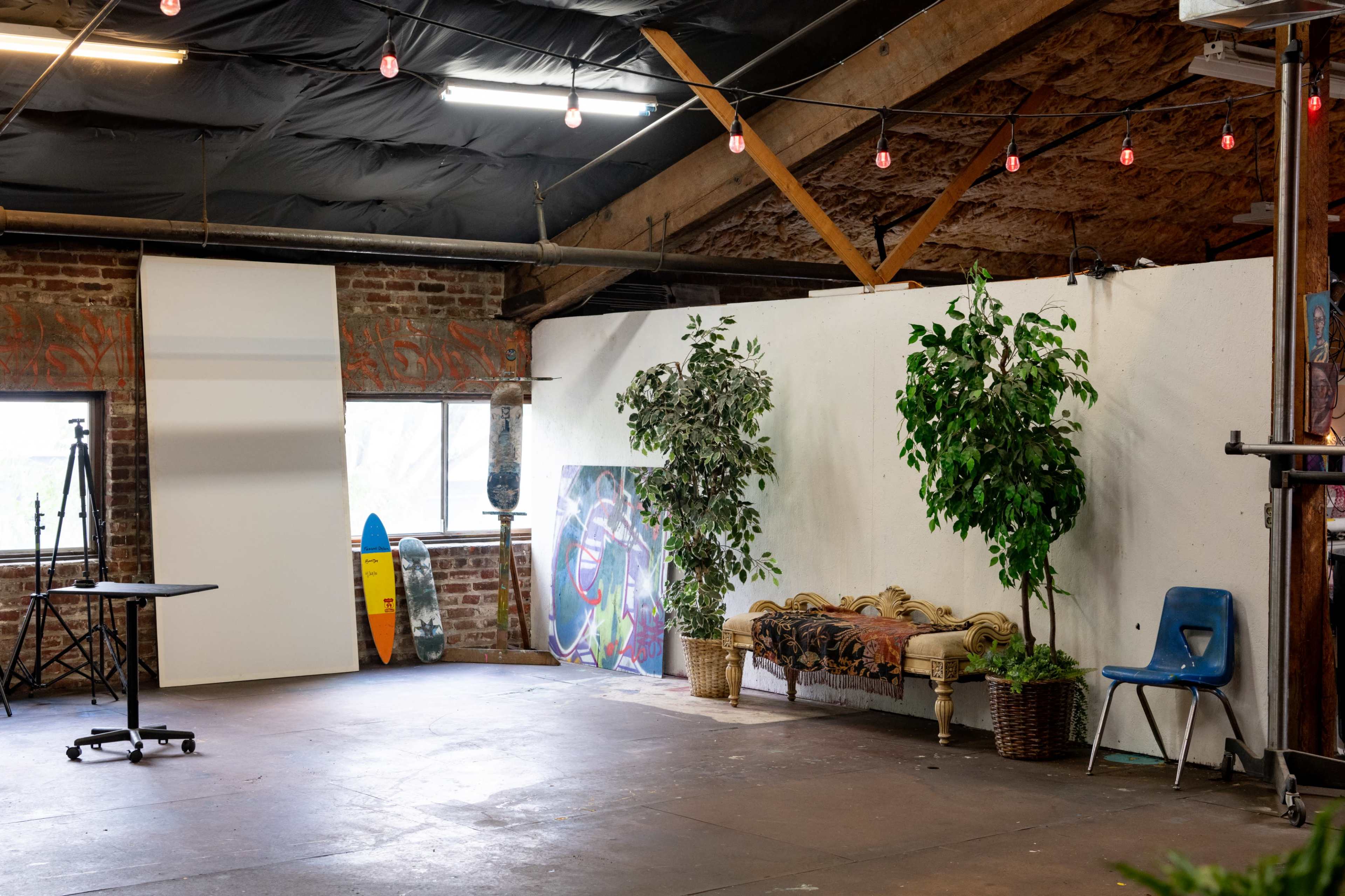 The image shows an industrial-style studio space with exposed brick walls, plants, and a seating area, along with photography equipment and colorful surfboards in the background.