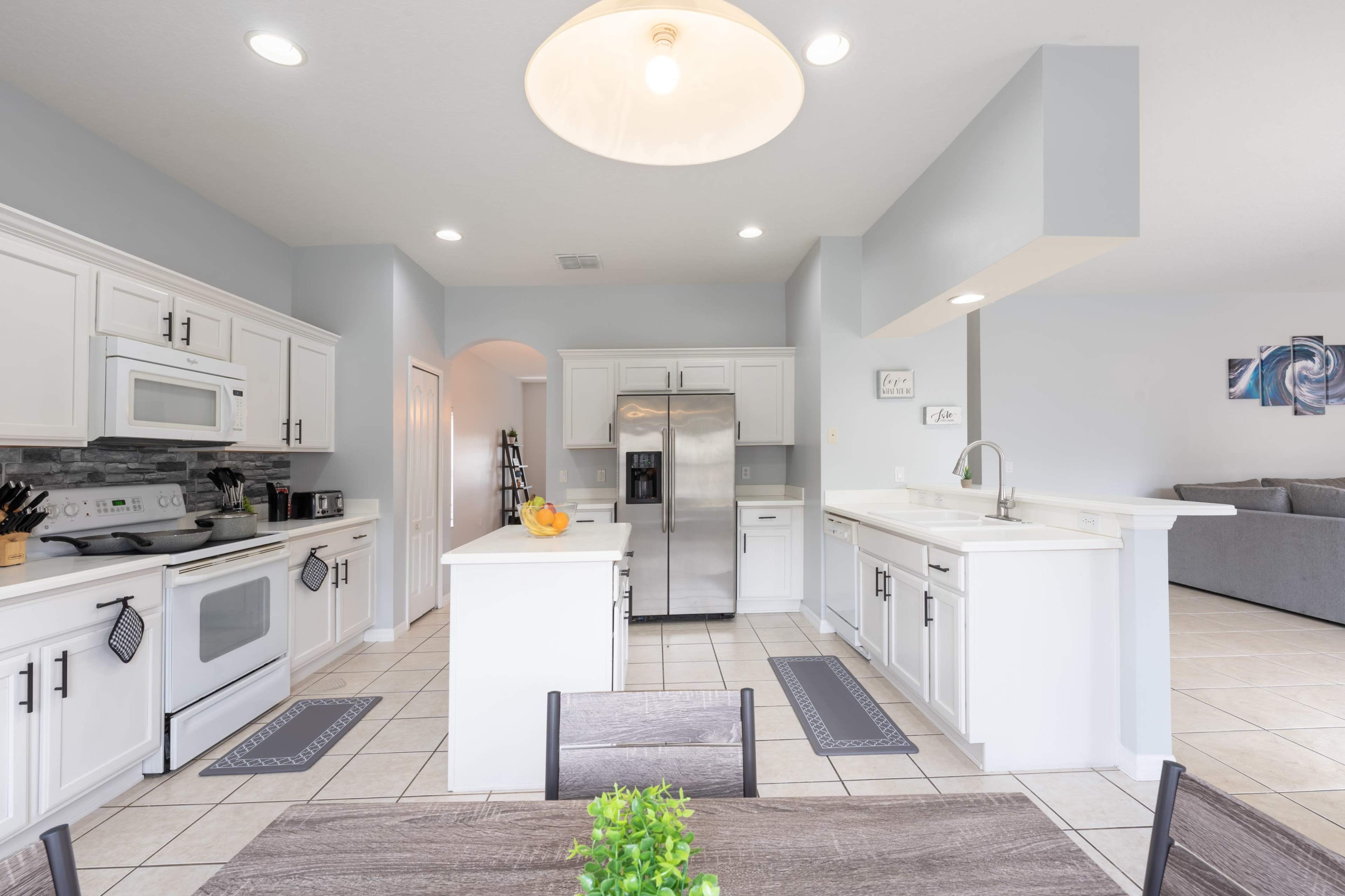 A modern kitchen features white cabinetry, stainless steel appliances, and a central island with bar seating.