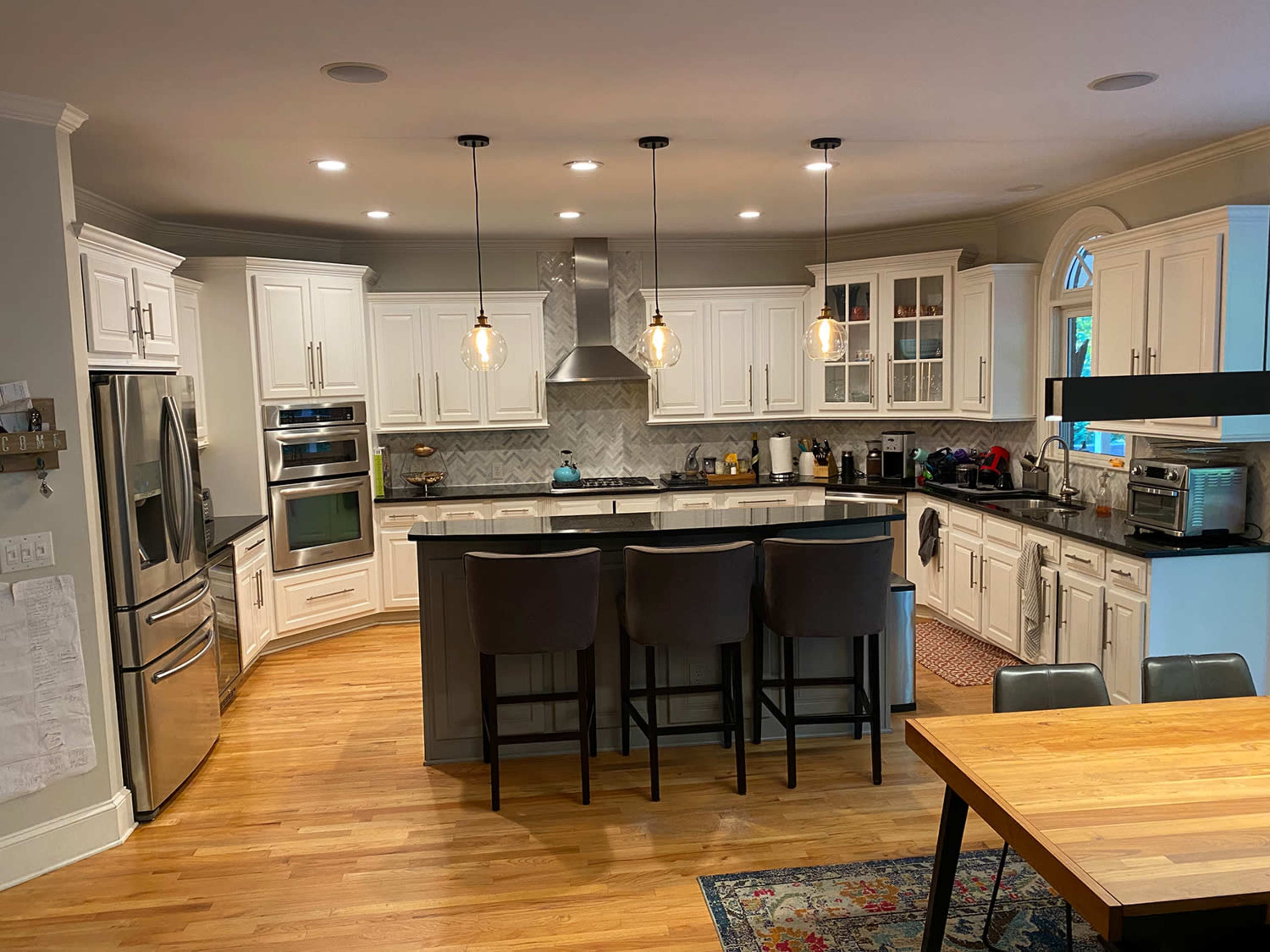 A modern kitchen featuring white cabinetry, stainless steel appliances, a central island with bar stools, and wooden flooring.