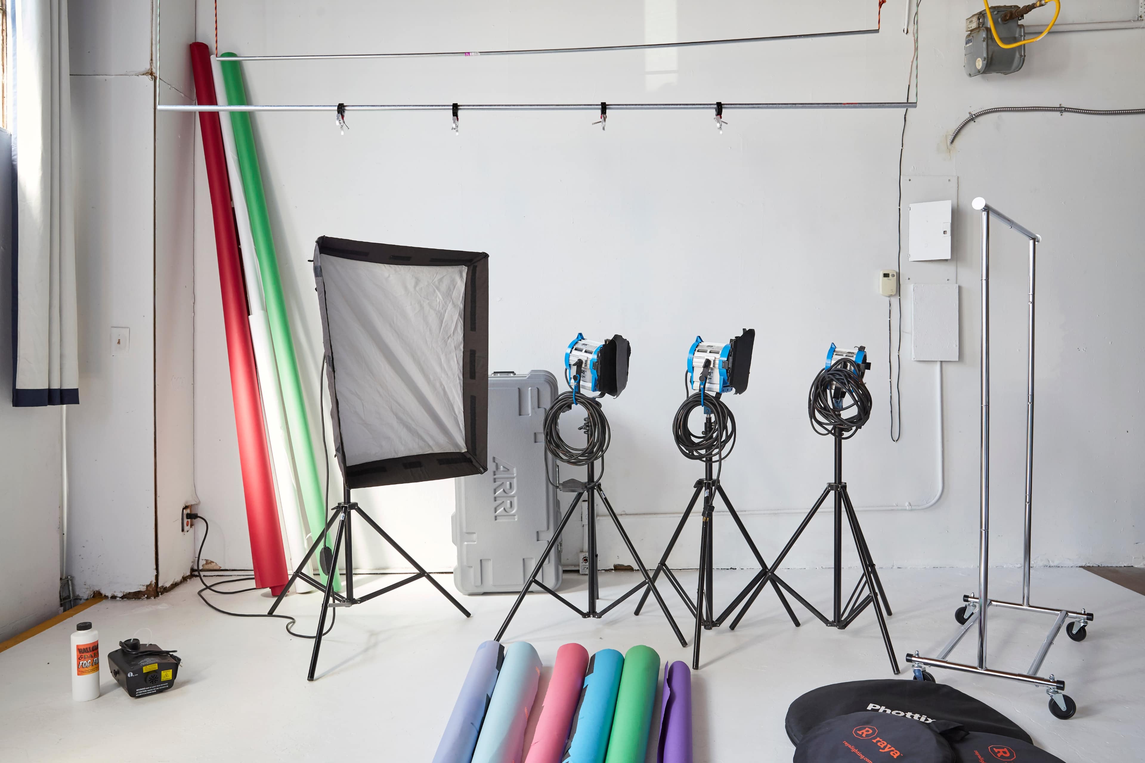 The image shows a photography studio with lighting equipment on stands, colorful backdrops, and a variety of props arranged on the floor.