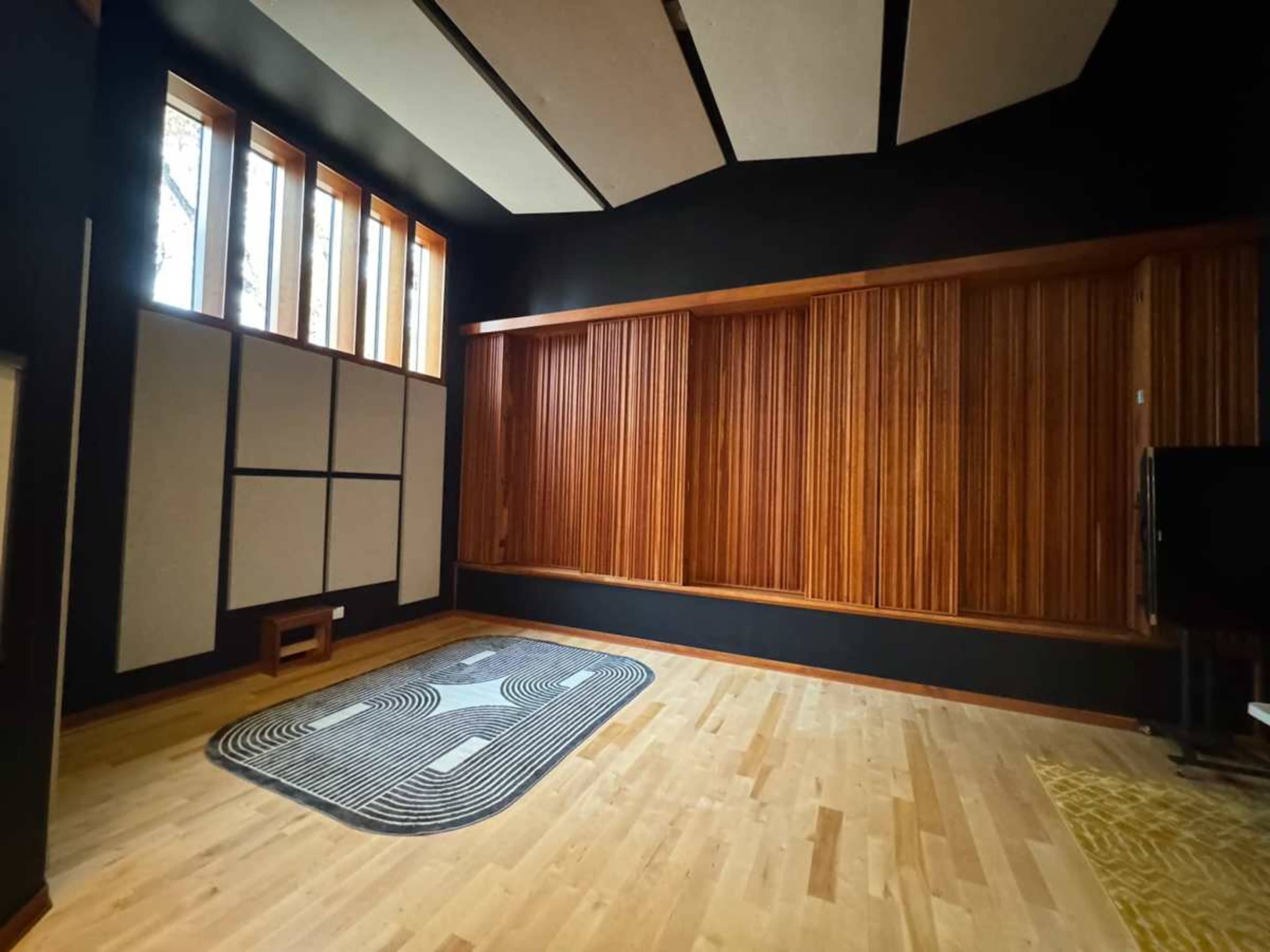 The image shows a room with hardwood flooring, large windows, and wooden panel walls, featuring acoustic treatment and various textures.
