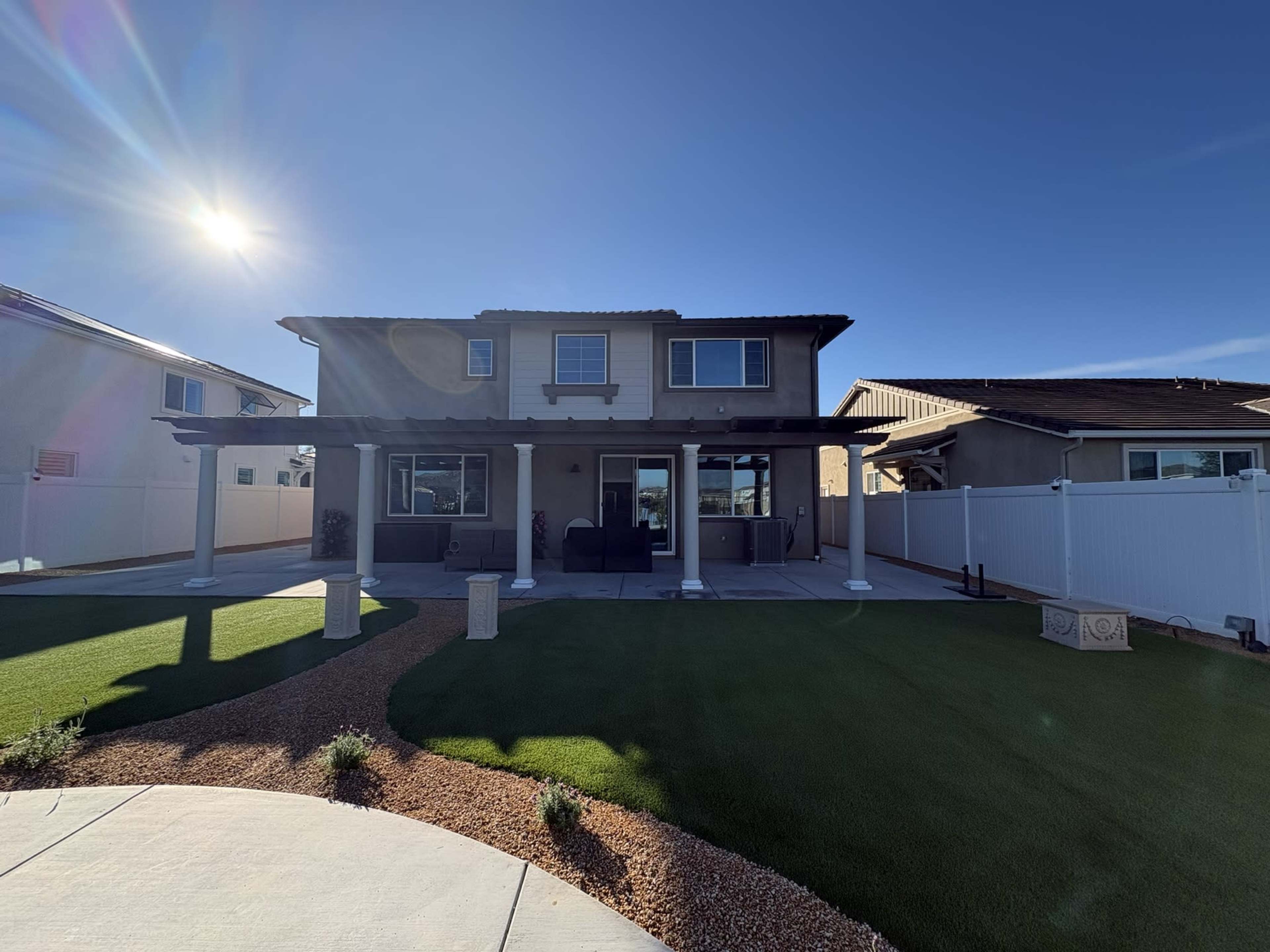 The image shows a two-story house with a covered patio and a well-maintained lawn, set against a clear blue sky.