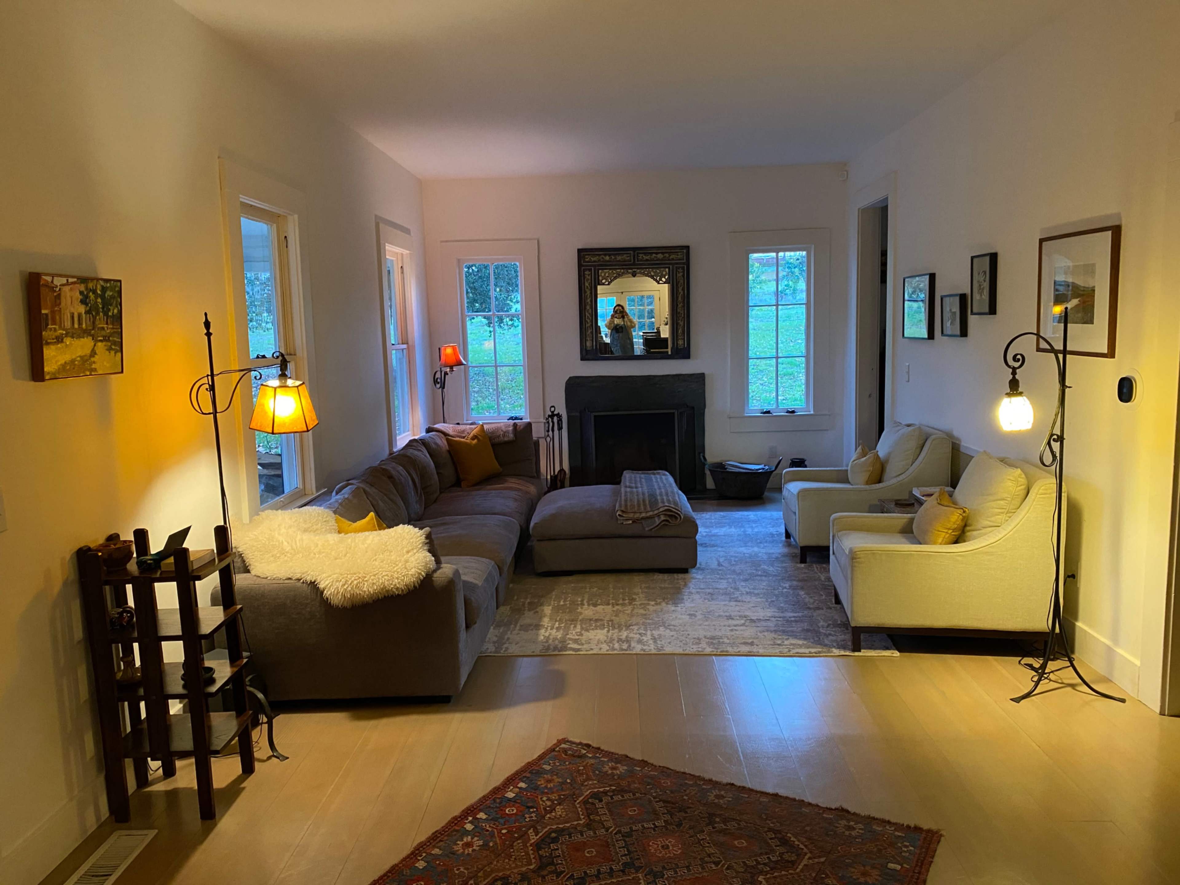 The image shows a cozy living room with a large sectional sofa, two armchairs, a fireplace, and windows that let in natural light.