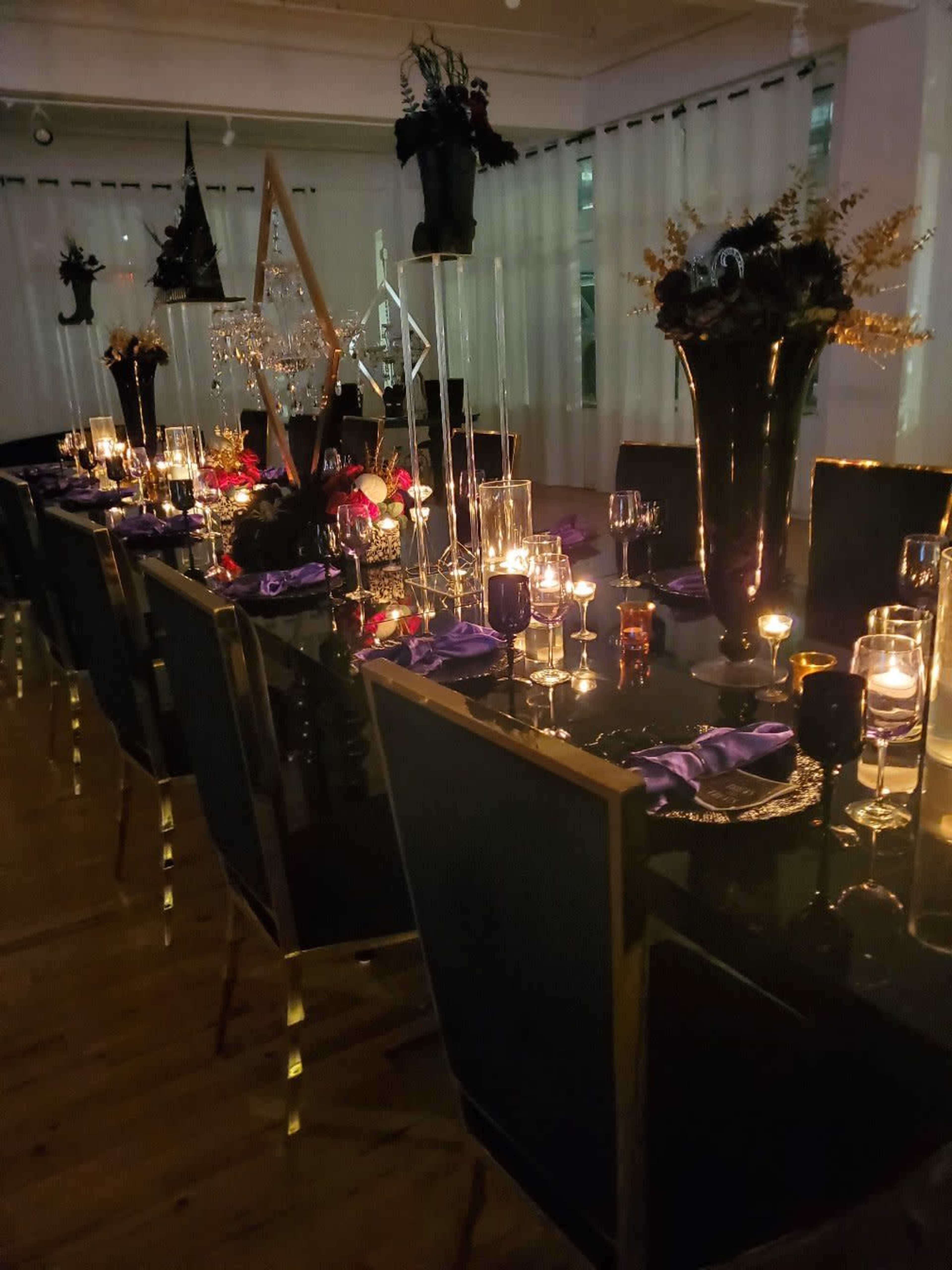 A long dining table is elegantly set with purple napkins, candles, and decorative centerpieces in a dimly lit environment.