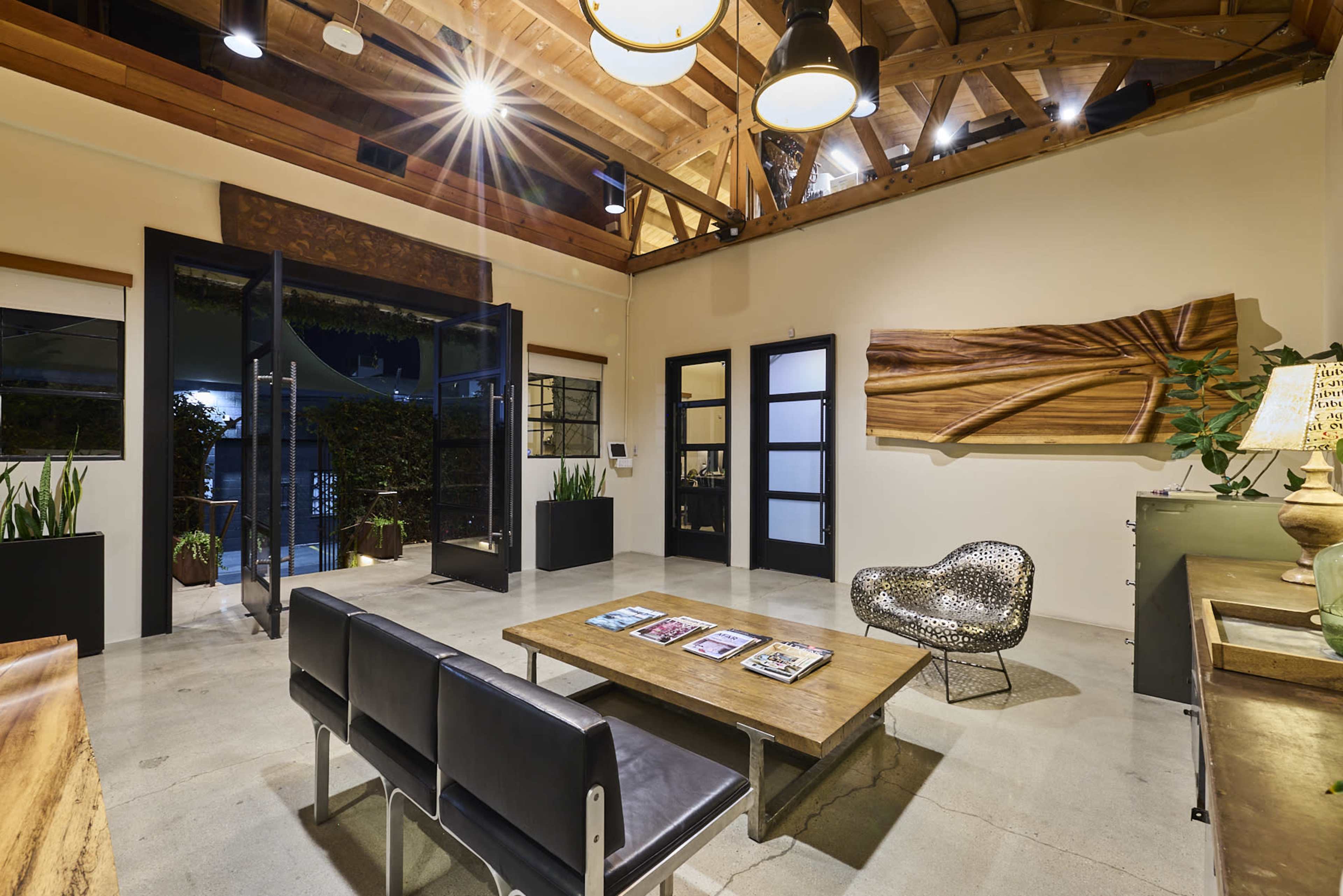 The image shows a modern reception area with a wooden coffee table, black chairs, and large glass doors leading to an outdoor space.