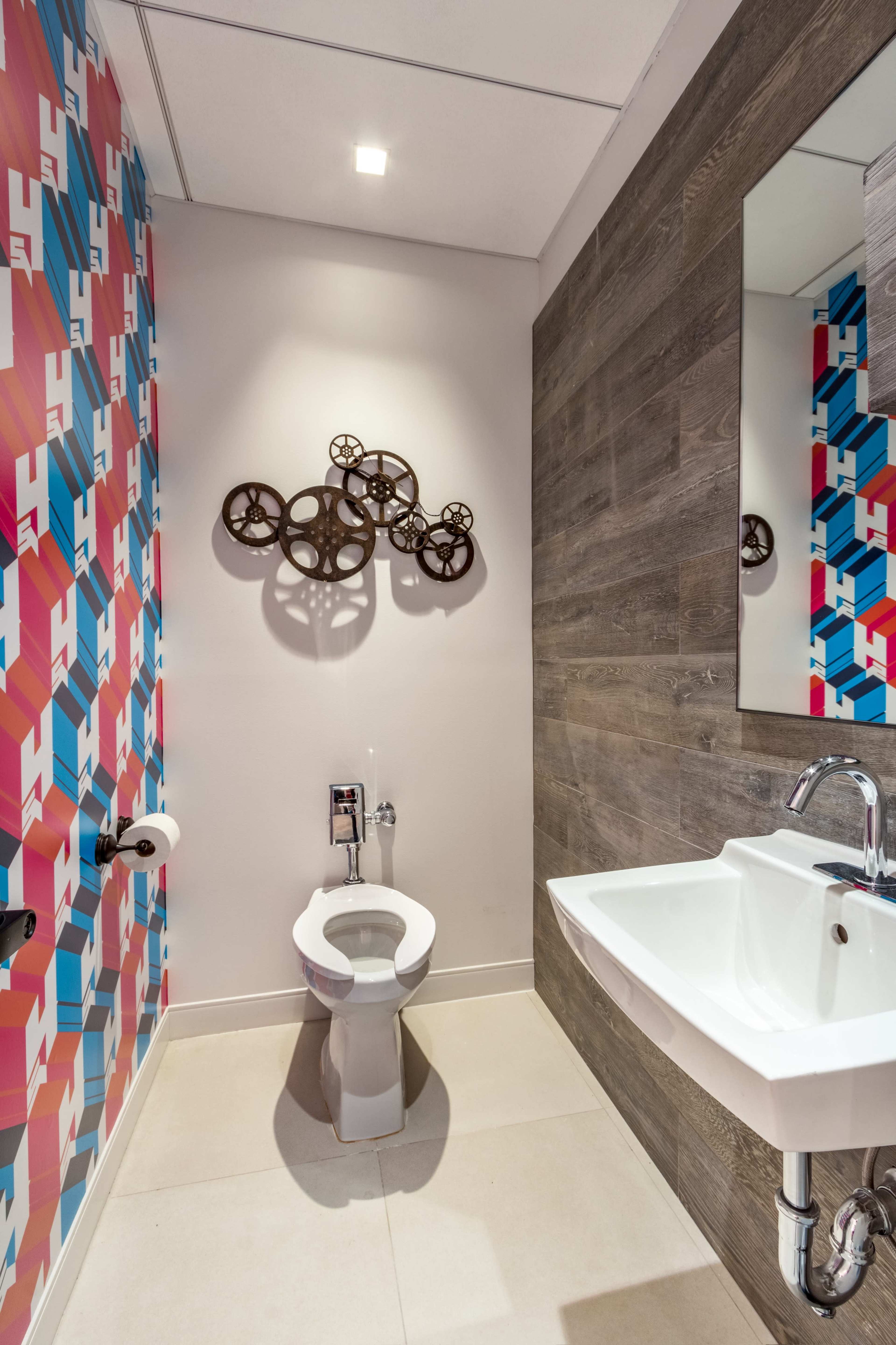 A modern bathroom with a colorful geometric wall design, a toilet, a sink, and decorative wall art made of gears.
