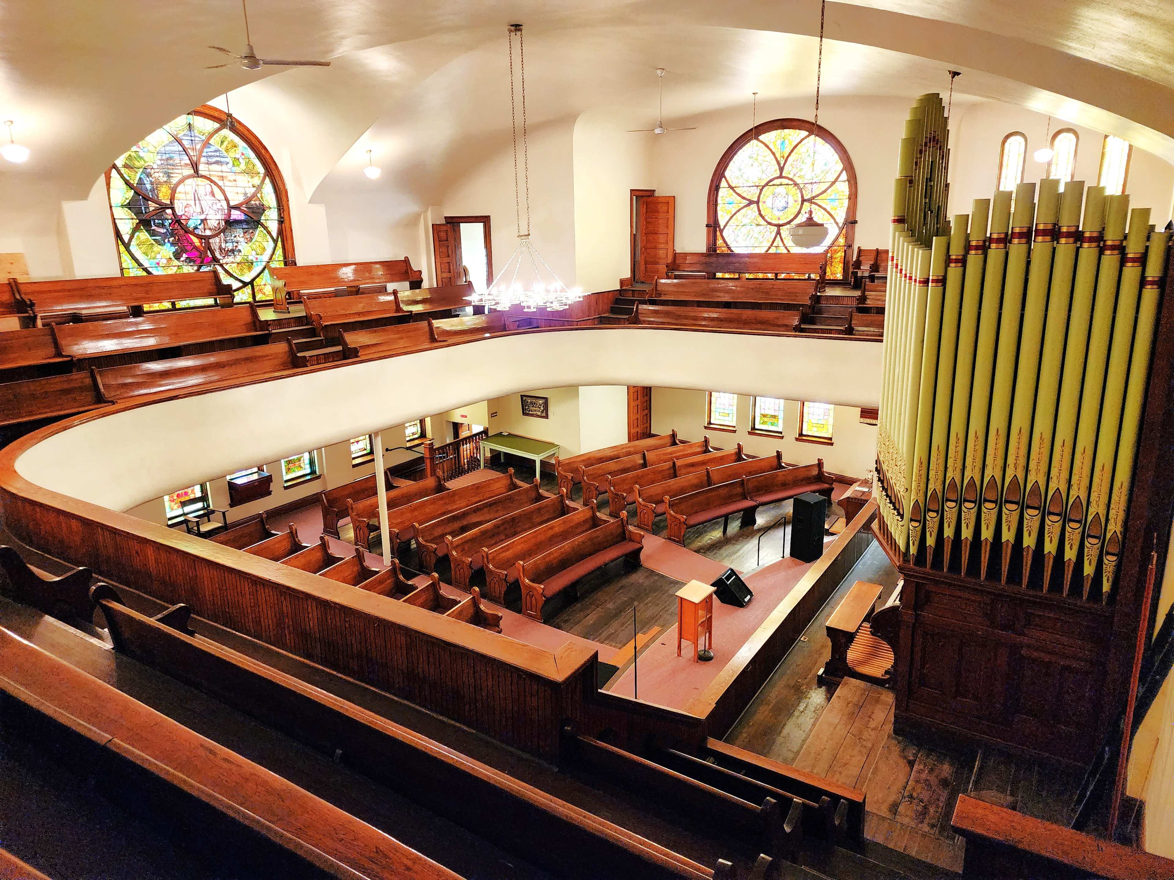 A spacious interior of a church with wooden benches, stained glass windows, and a large pipe organ on one side.