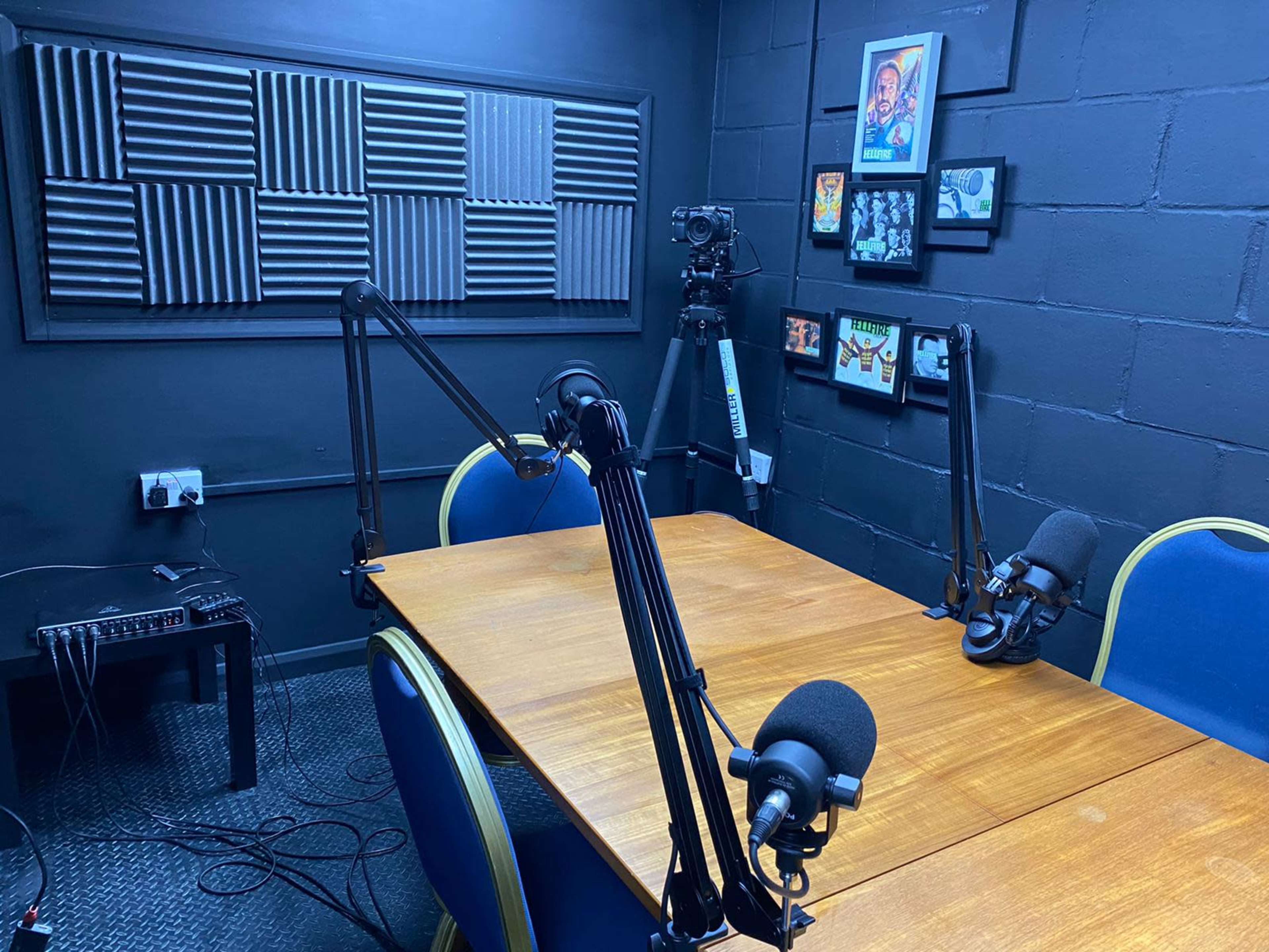 A podcast recording studio with a wooden table, two microphone stands, and soundproofing panels on the walls.