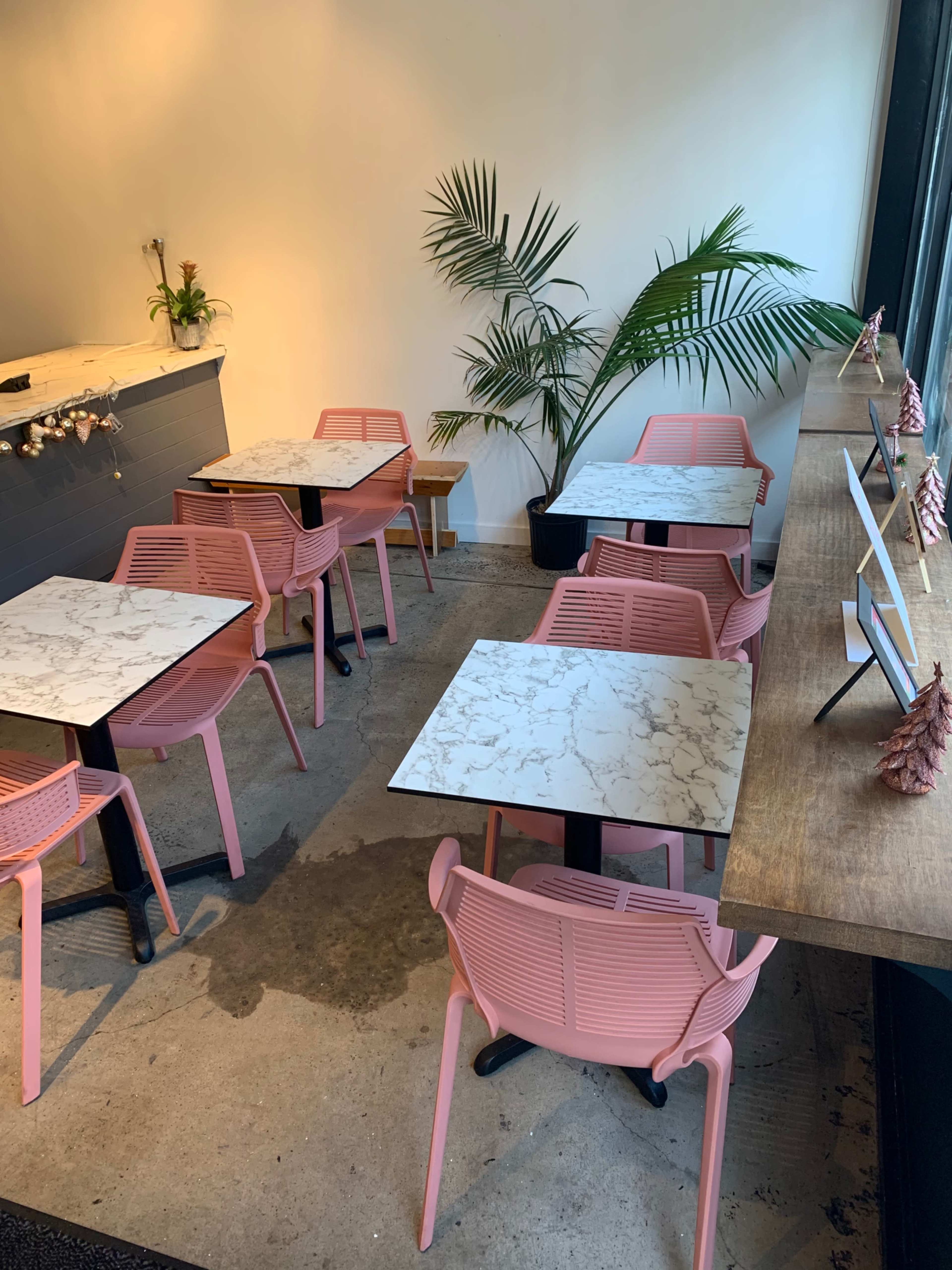 A cafe interior with pink chairs arranged around marble-top tables and a wooden counter with decorative items.