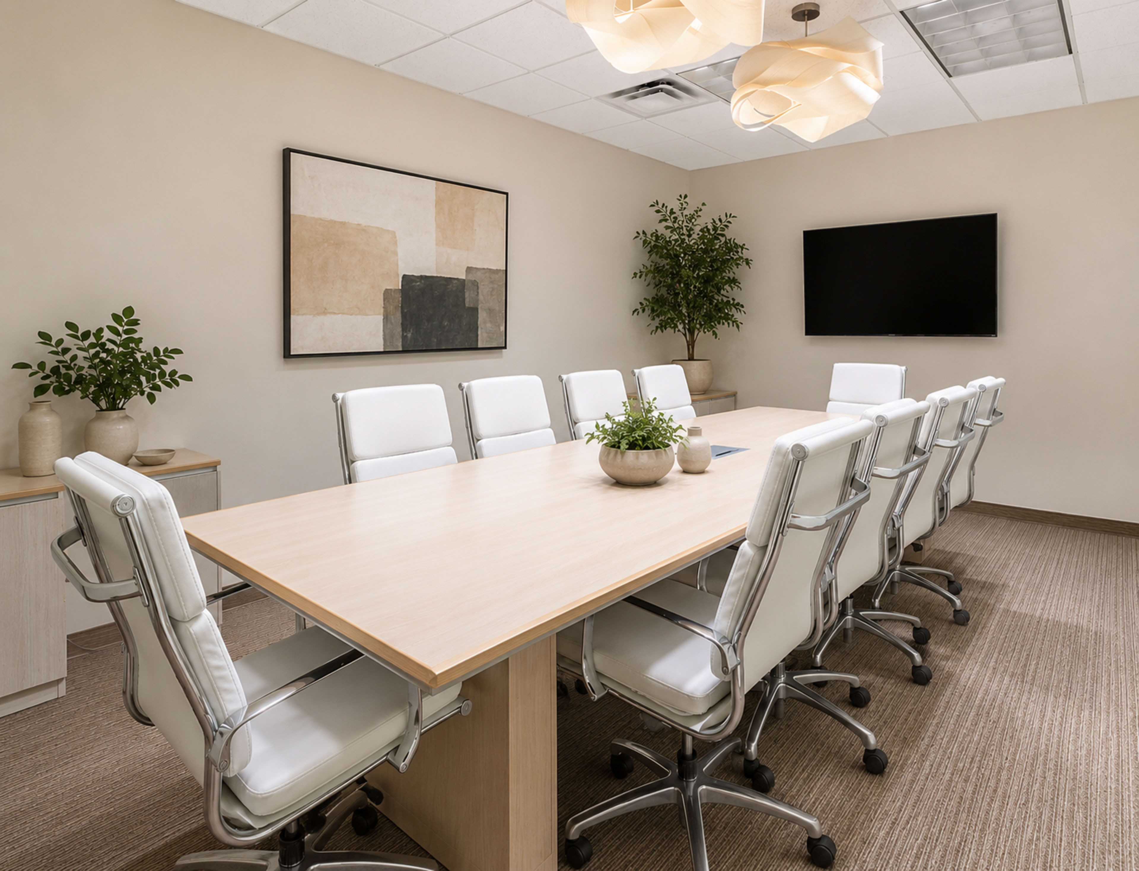 A modern conference room features a long wooden table surrounded by white ergonomic chairs, with plants and a wall-mounted screen enhancing the space.