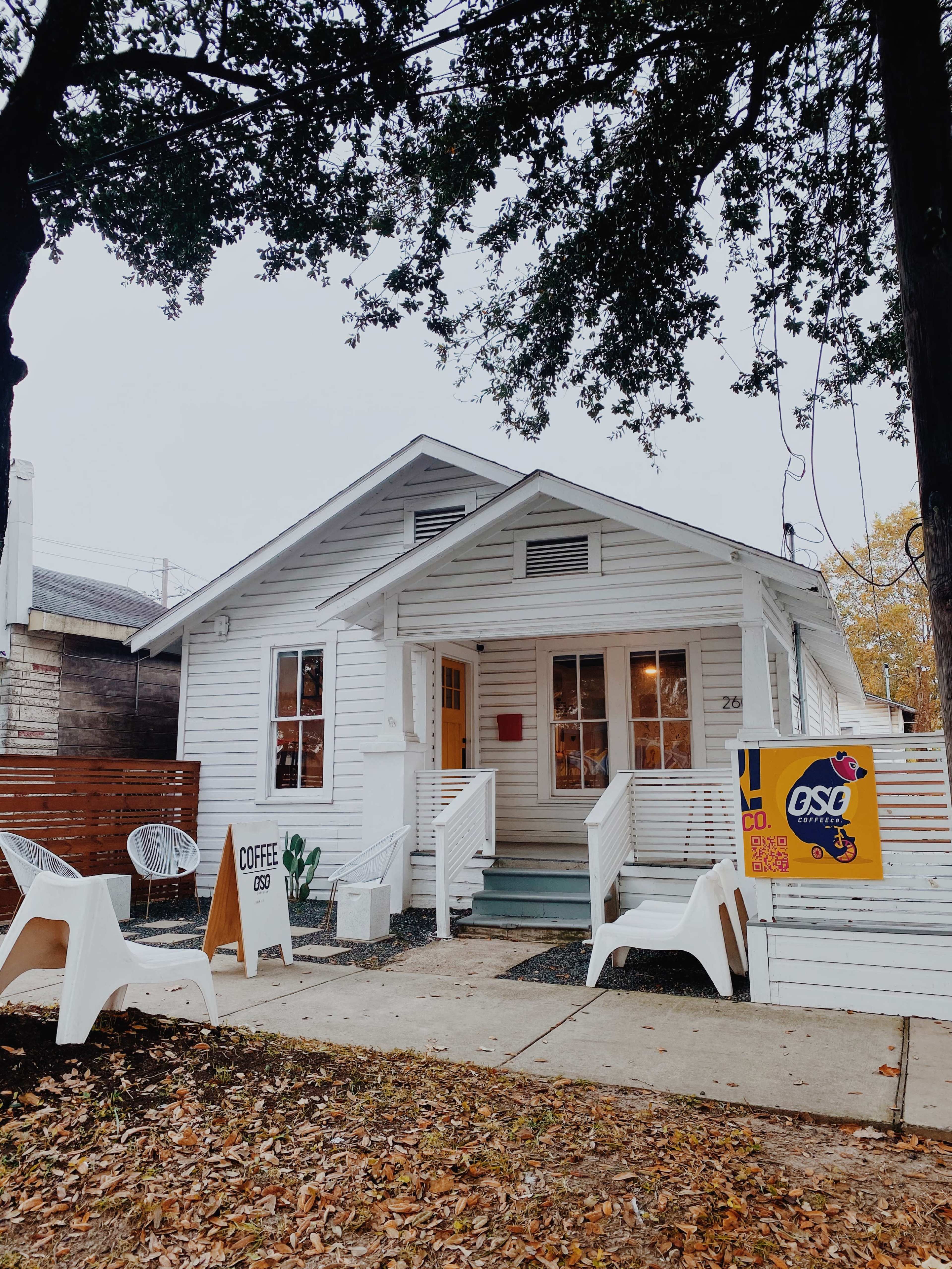 A white, single-story house with a porch features a sign advertising coffee and outdoor seating in front.
