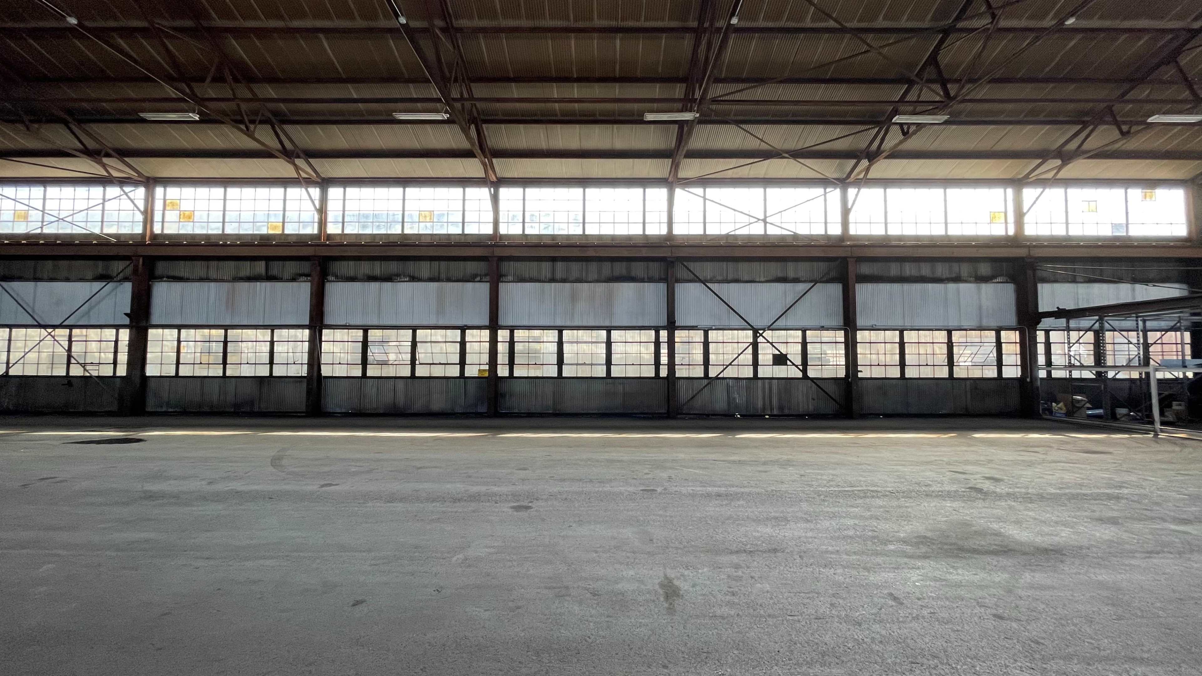 The interior of a spacious industrial warehouse with large windows providing natural light.