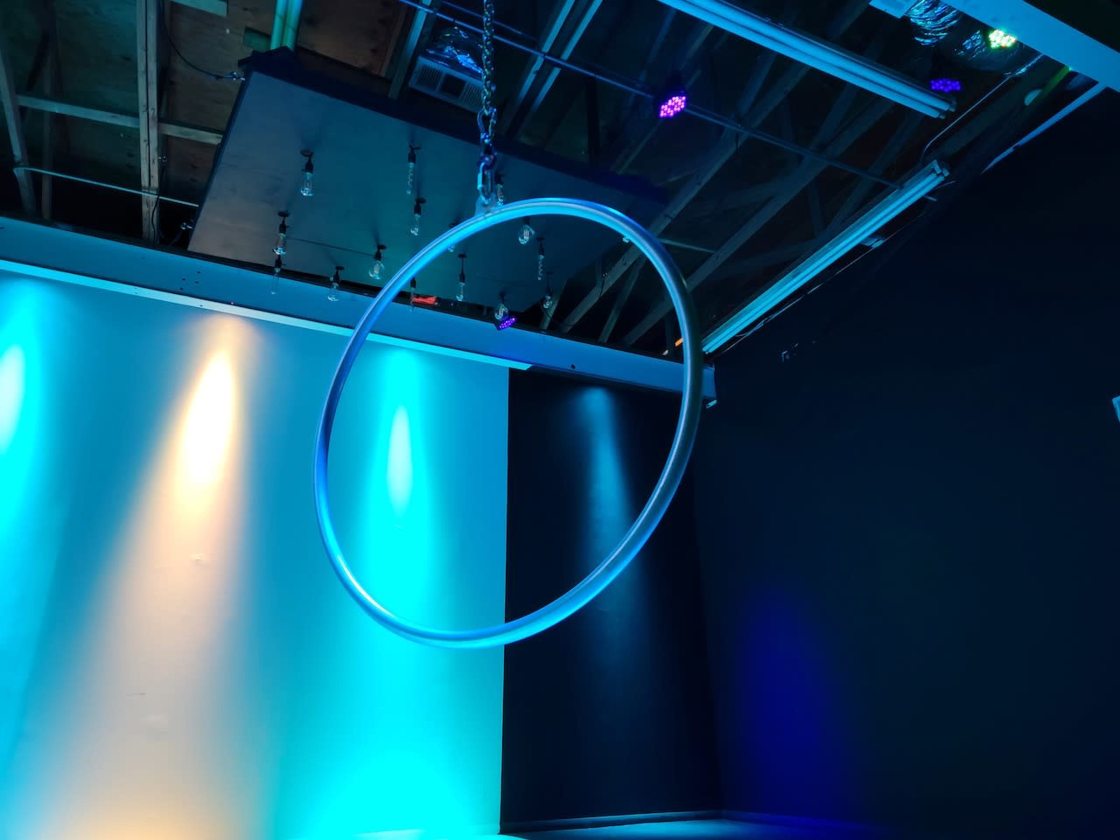 A large, illuminated hoop hangs from the ceiling in a studio space with colored lighting.