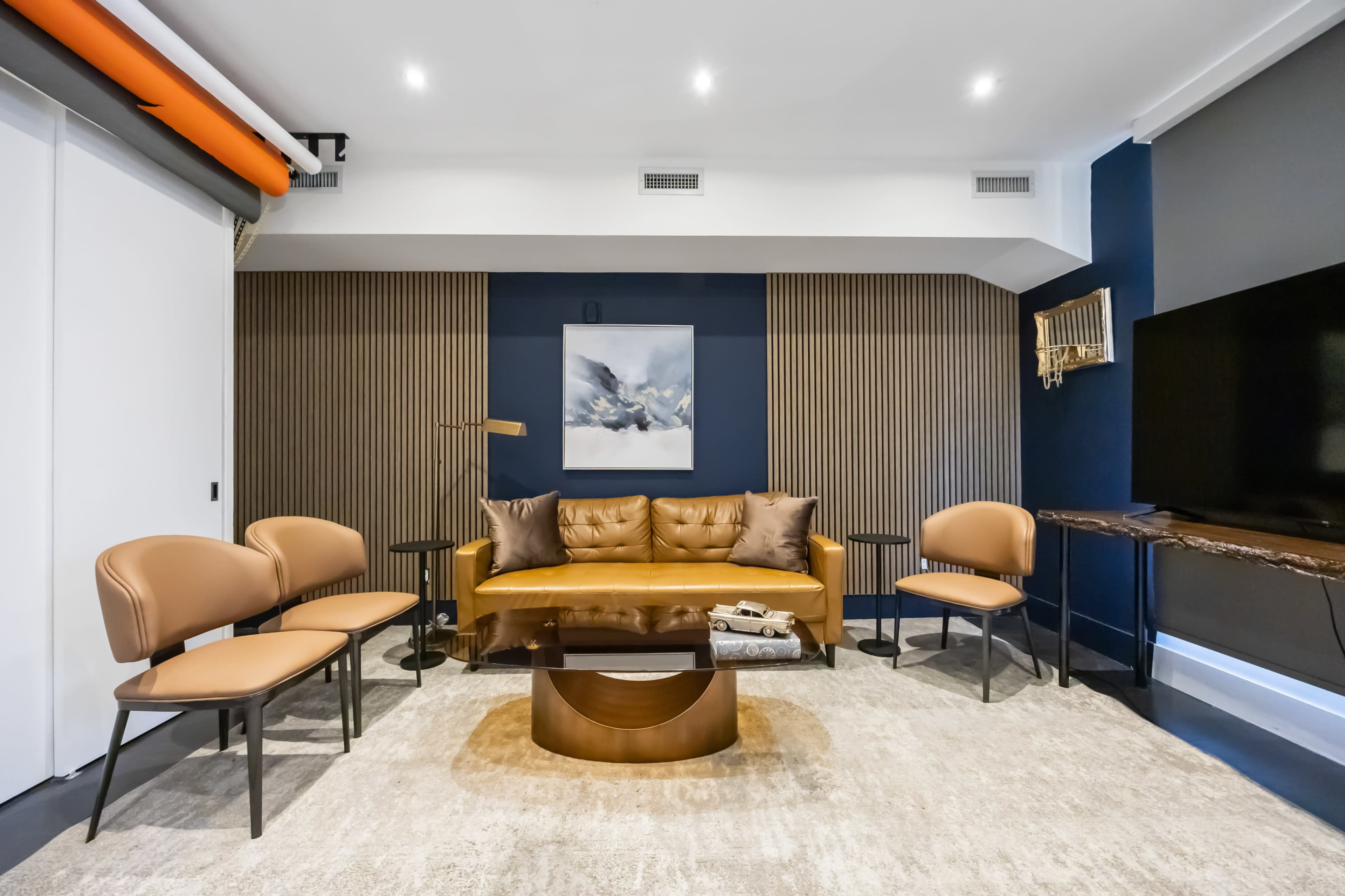The image shows a modern living room with a brown leather sofa, four chairs, a coffee table, and a piece of abstract art on the wall.