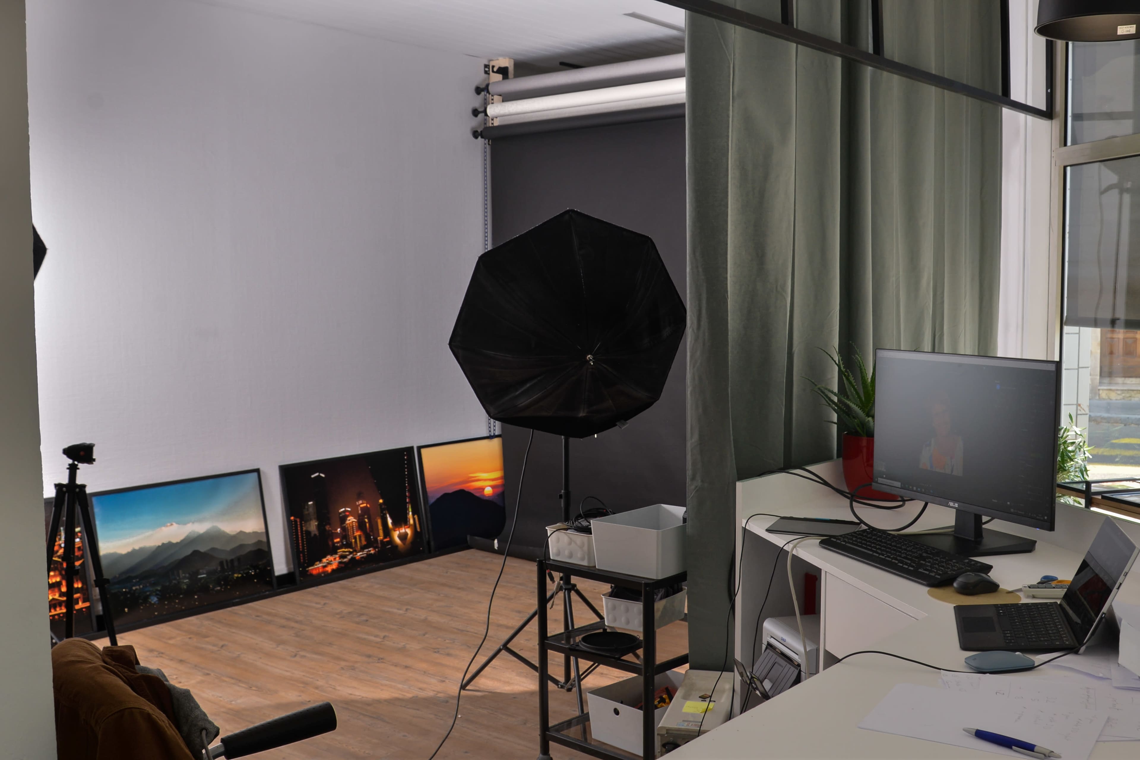 A photography studio with a backdrop setup, lighting equipment, and a desk with a computer.