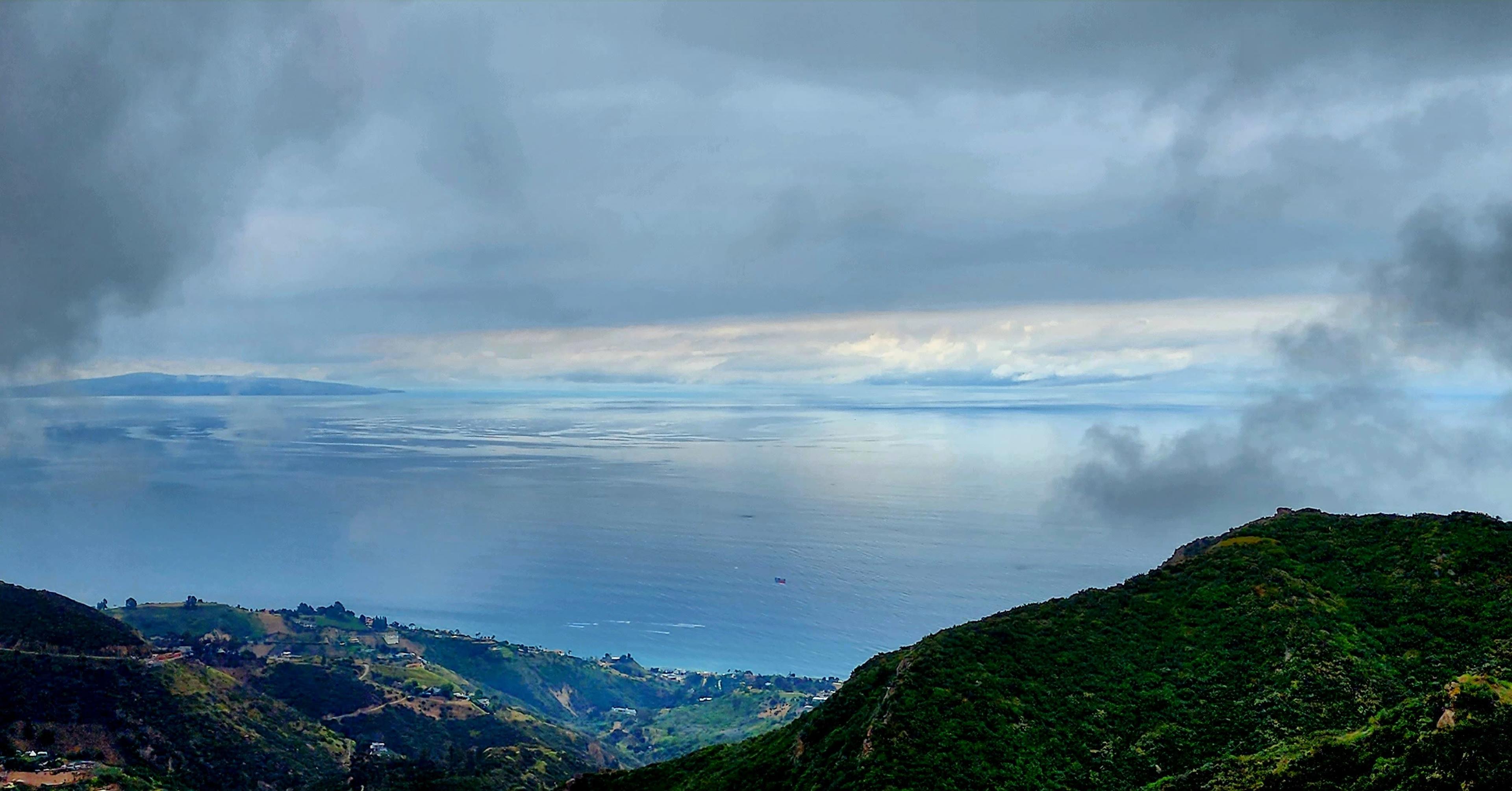 A cloudy sky overlooks a calm ocean with distant land visible on the horizon.