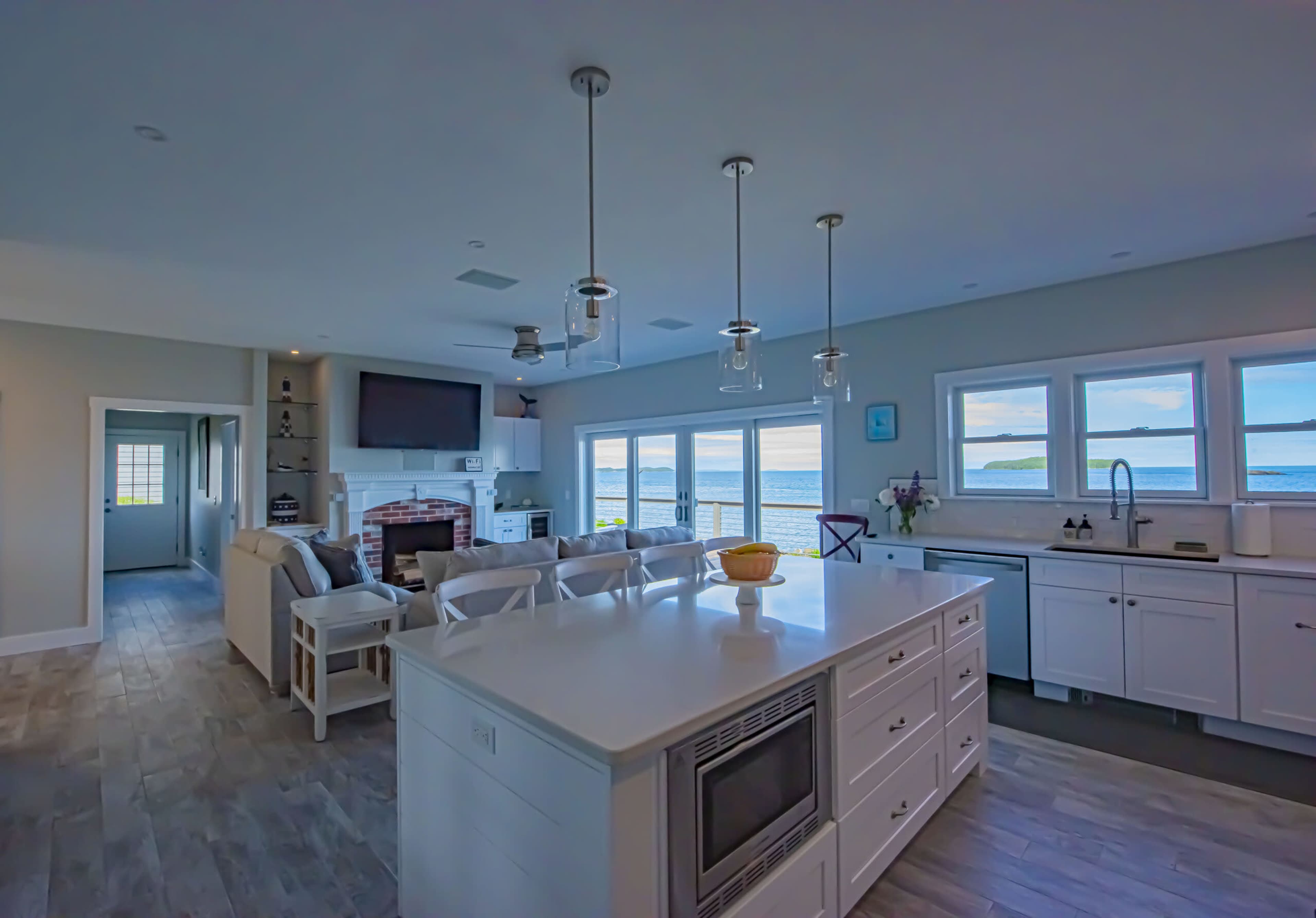 The image shows a modern kitchen with an island, white cabinetry, and large windows overlooking a waterfront view.