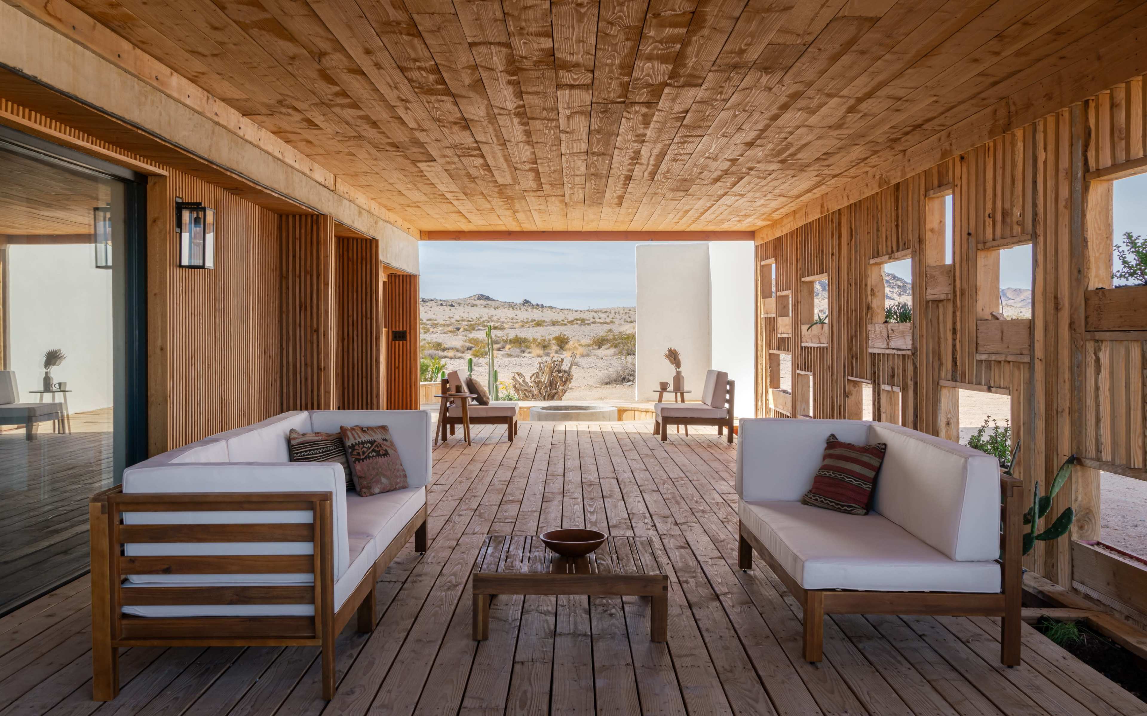A wooden porch features minimalist seating and a view of a desert landscape through an open doorway.
