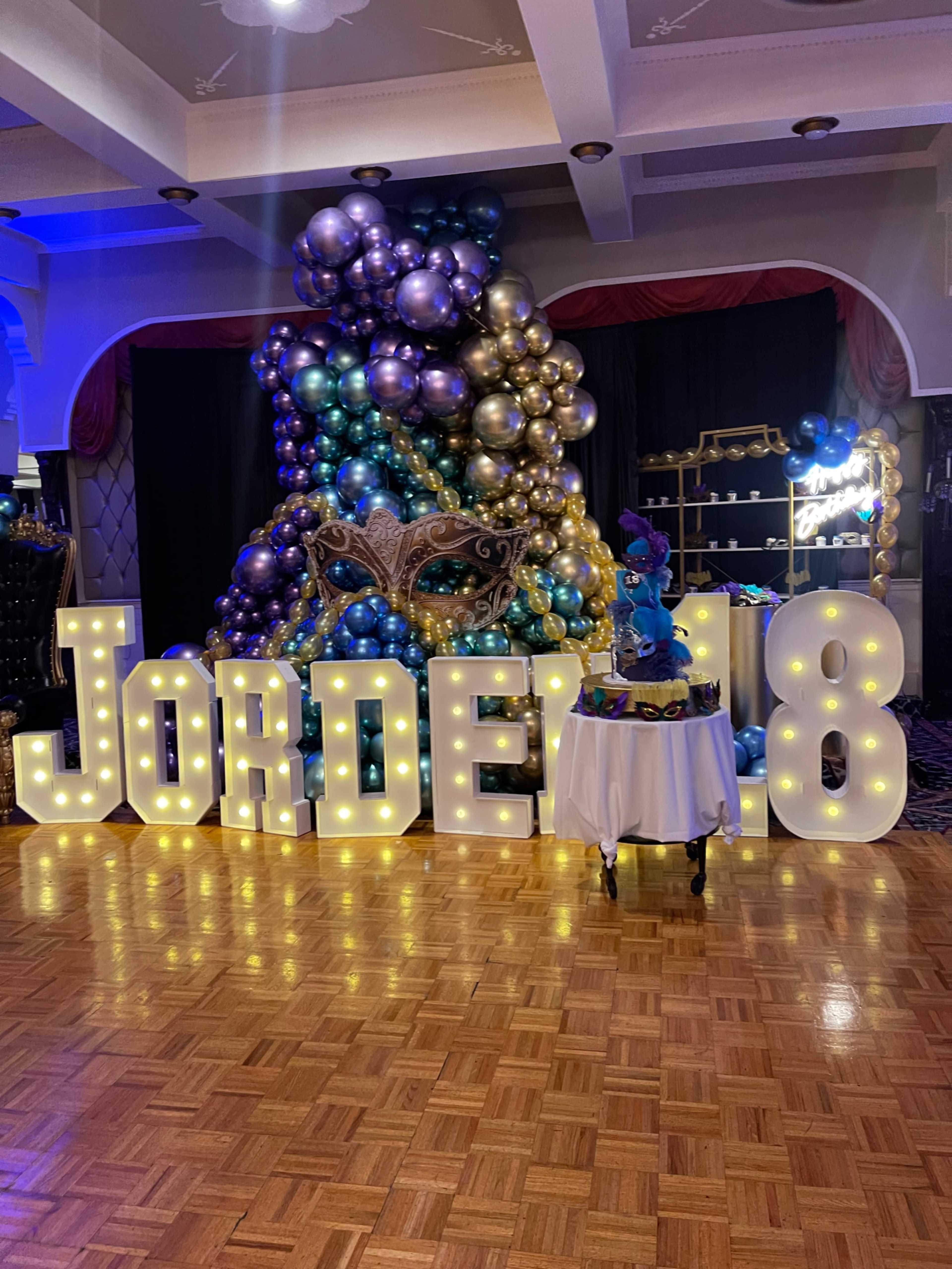 The image features a decorated party scene with large, illuminated letters spelling "Jordel 18" and a colorful balloon display in the background.