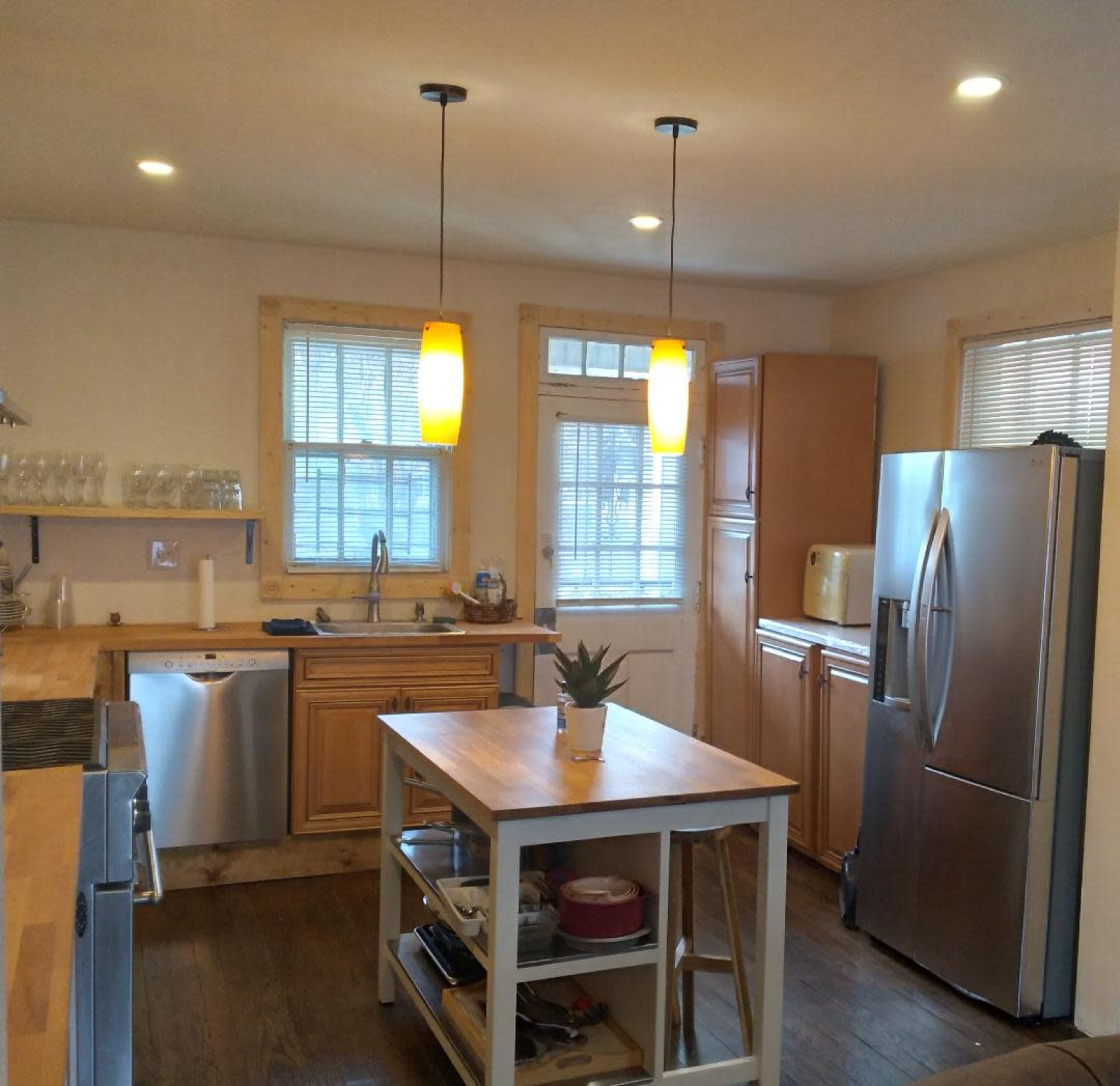 A modern kitchen featuring wooden cabinets, stainless steel appliances, and an island with a small potted plant on it.