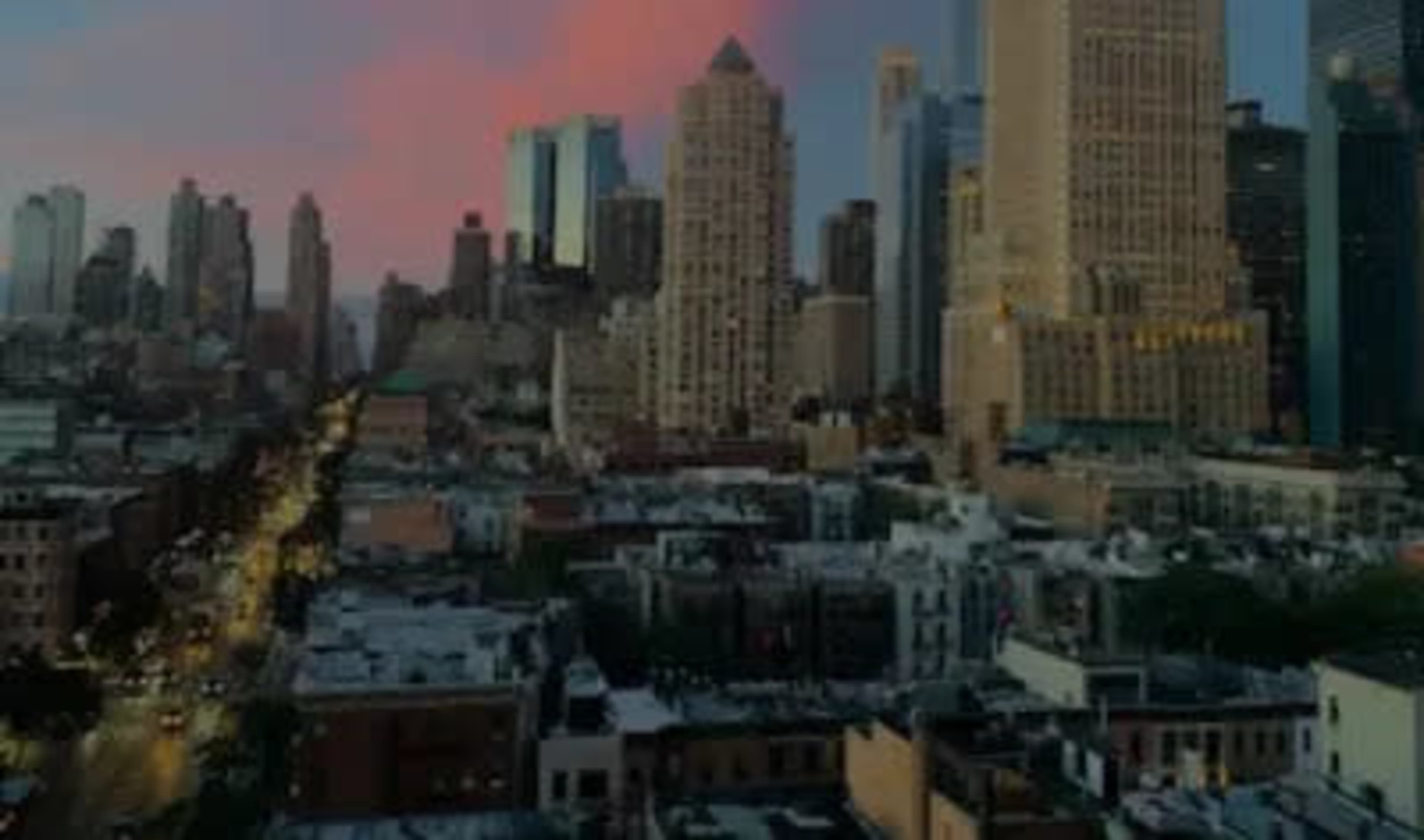 A skyline of tall buildings against a pastel sunset, with a bustling urban street below.