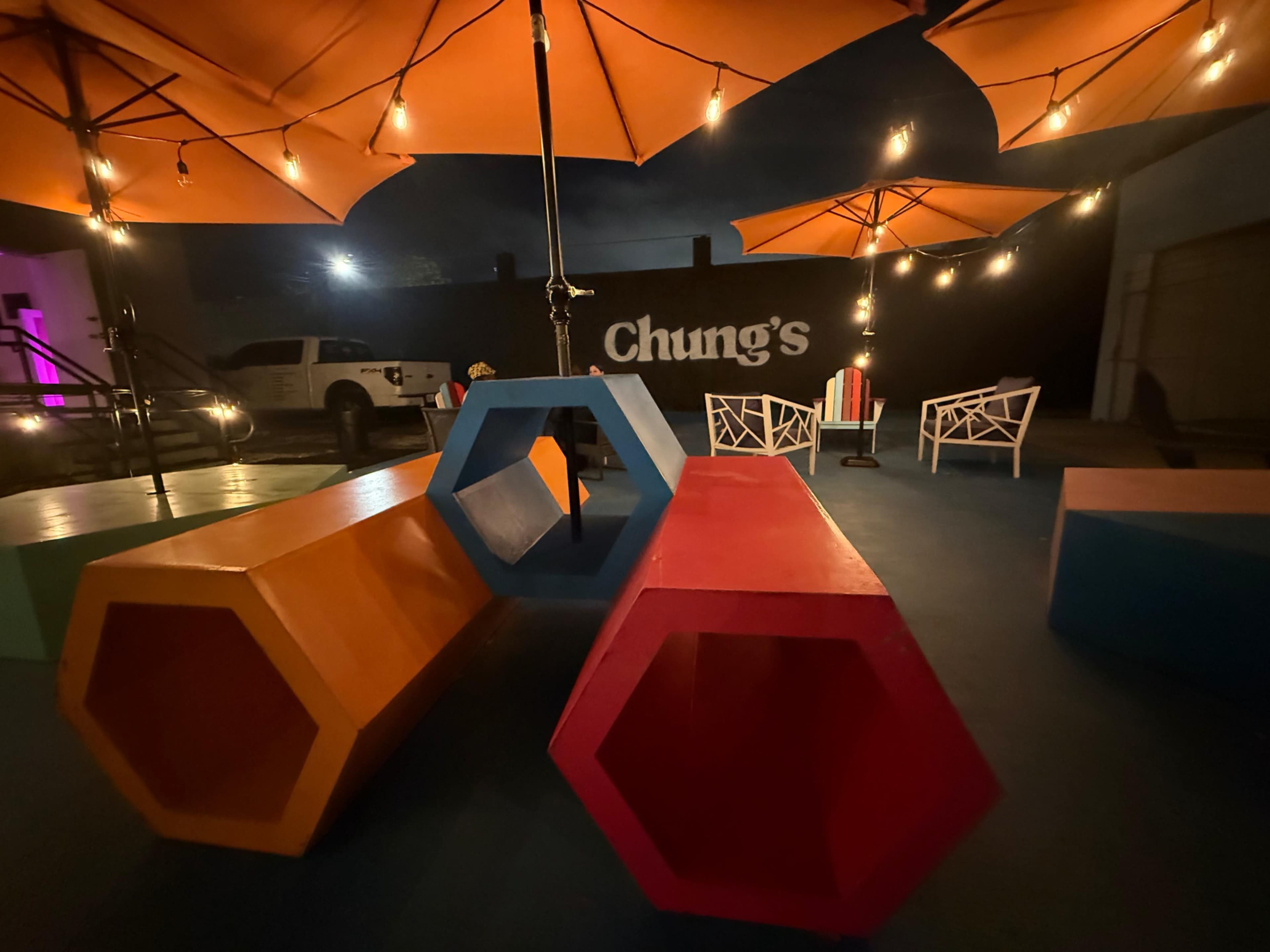 The image shows a colorful outdoor seating area with hexagonal benches under orange umbrellas at a venue named "Chung's."