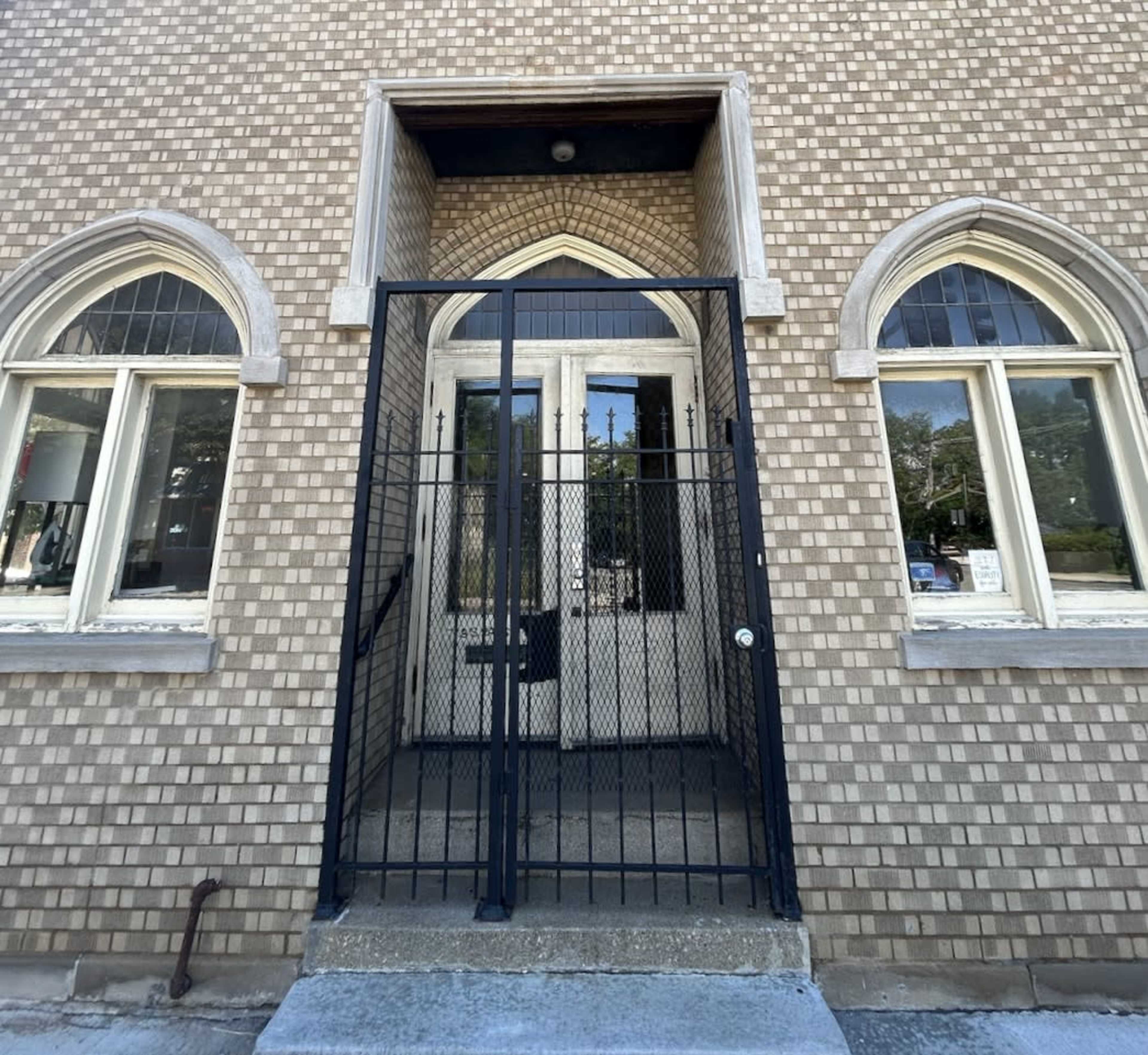The image shows a gated entrance with arched windows and a textured brick exterior.