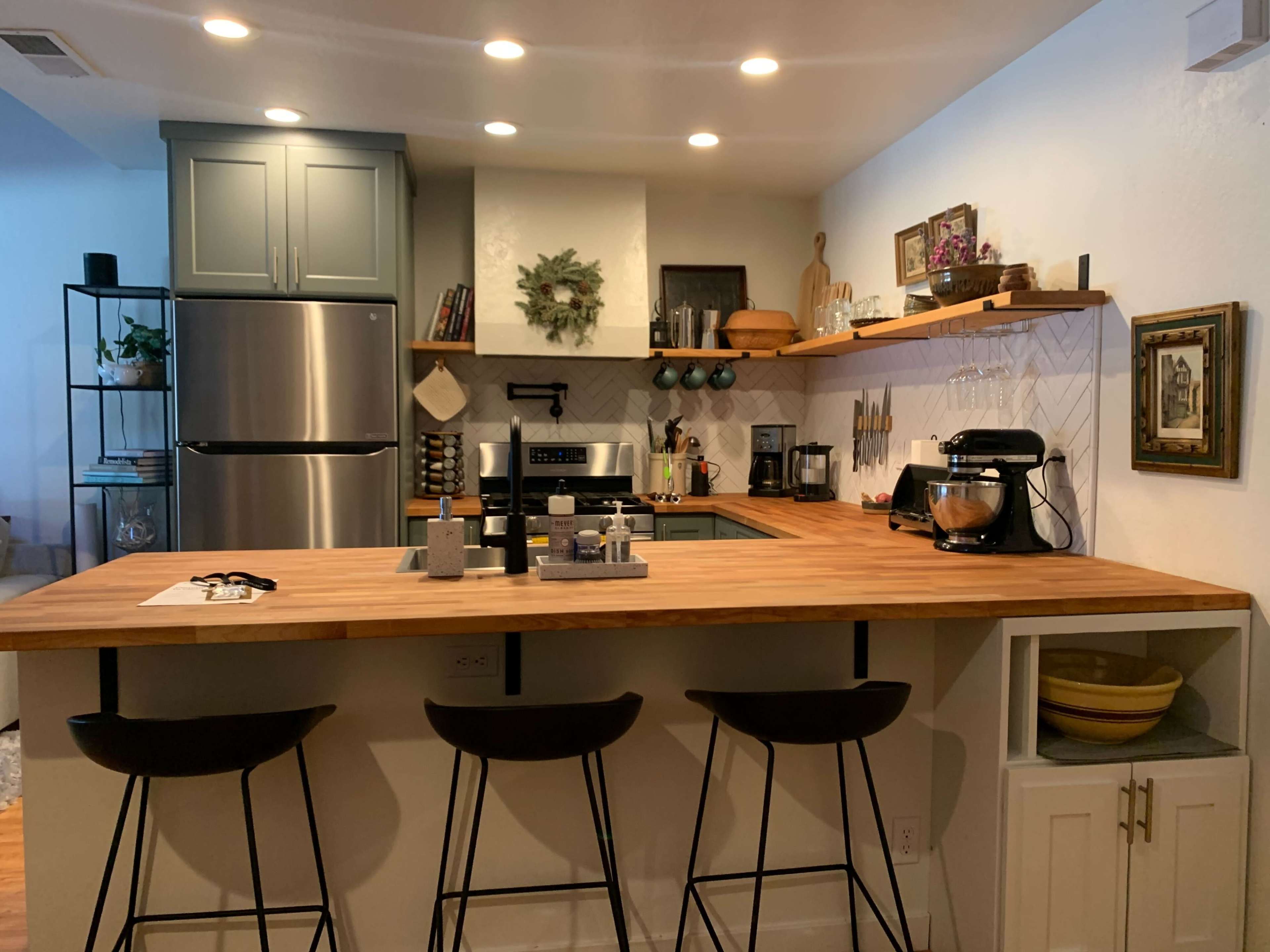 A modern kitchen with a wooden countertop, stainless steel appliances, and bar stools.