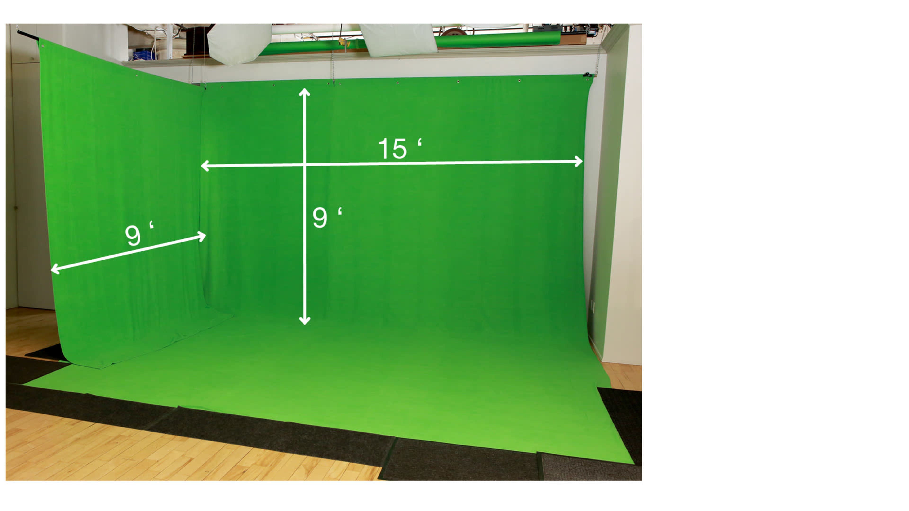 A green screen setup with dimensions indicated: 15 feet wide and 9 feet tall, placed on a floor with mats.