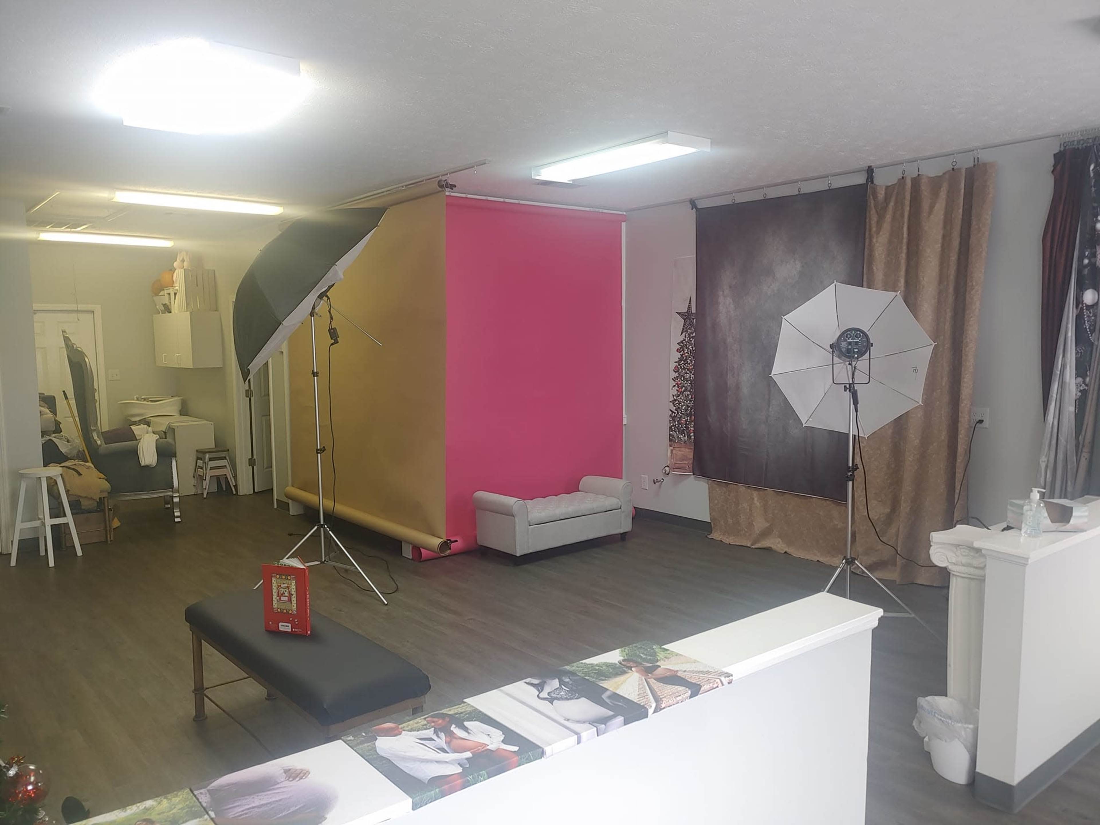 A photography studio with a pink accent wall, two lighting setups, a gray sofa, and a backdrop draped in fabric.