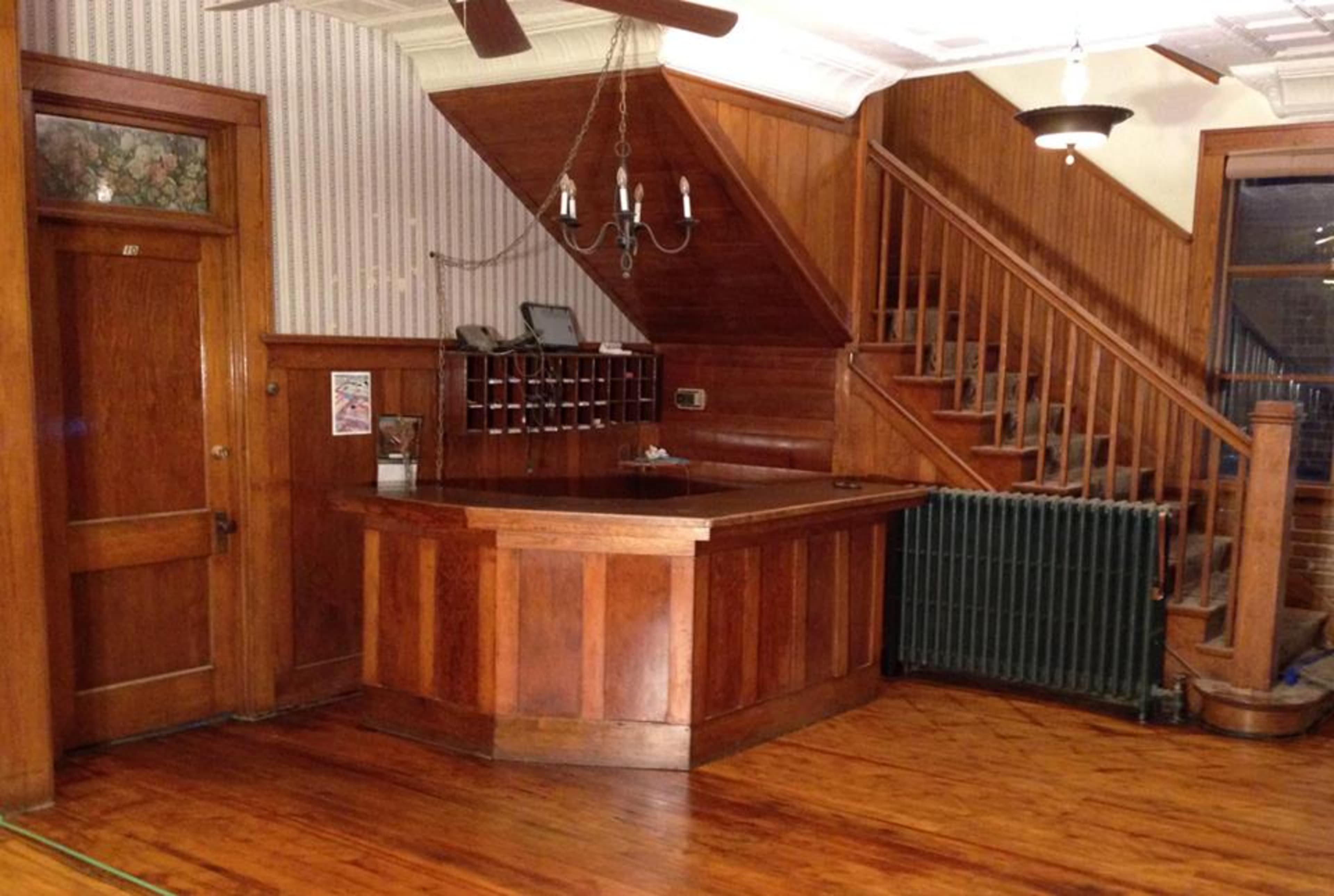 A wooden reception area with a counter, a staircase in the background, and a radiator along the wall.