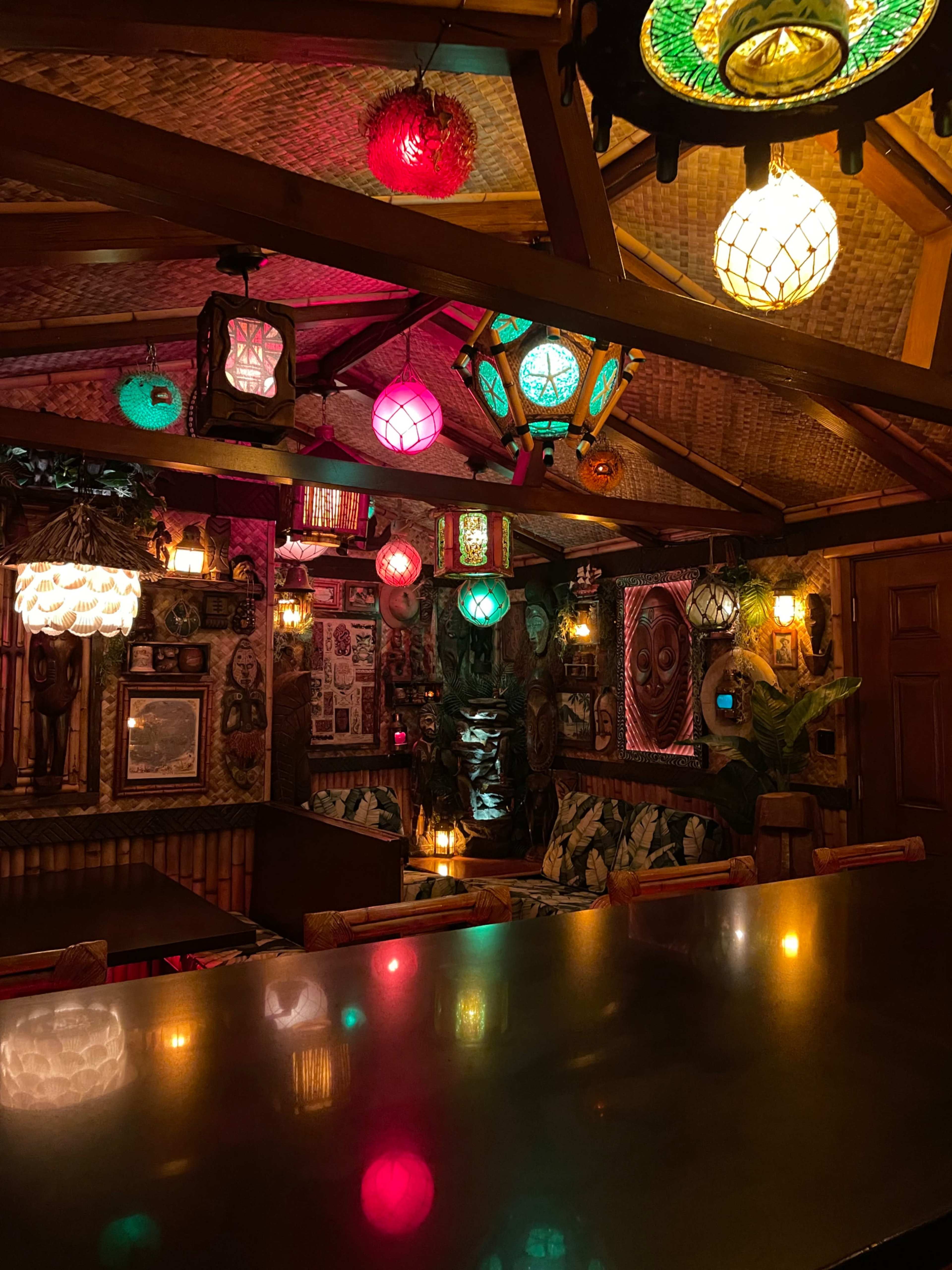 The interior of a tiki-themed bar features colorful lanterns hanging from the ceiling and vintage decorations on the walls.
