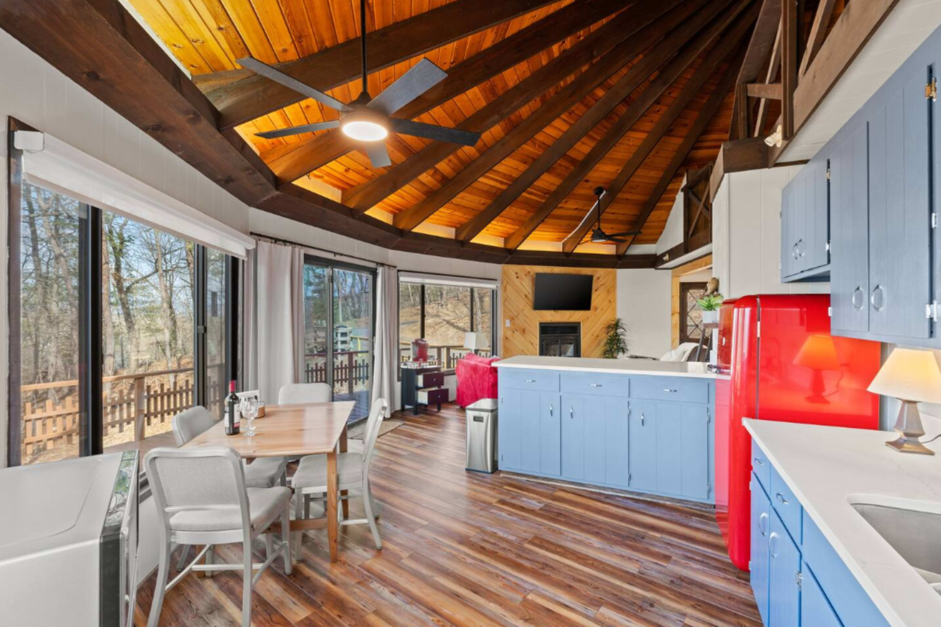 The image shows a circular kitchen and dining area with wooden beams, large windows, and a red refrigerator.