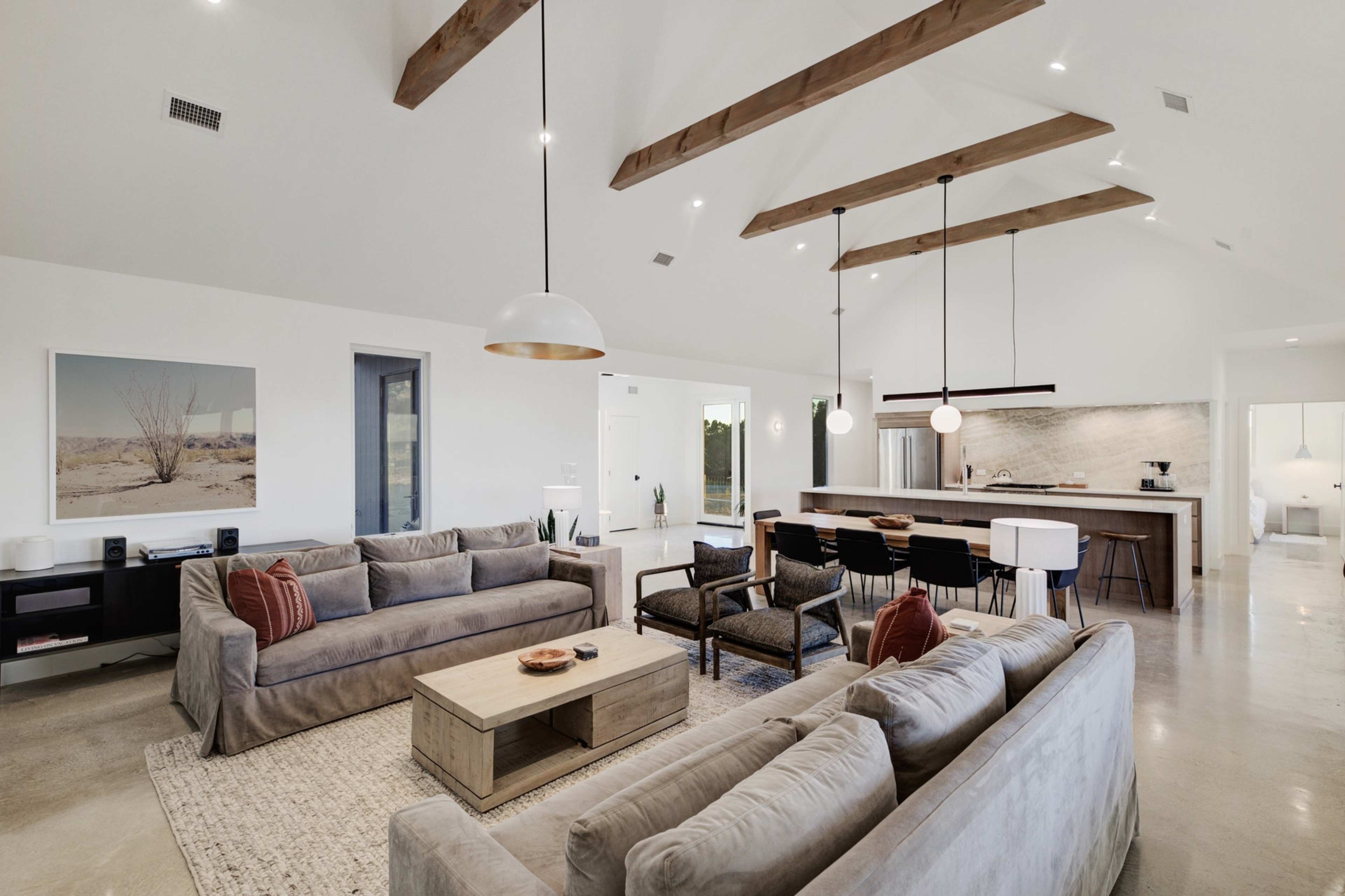 A modern living room with two large gray sofas, a coffee table, and a kitchen area in the background featuring a spacious island and bar seating.