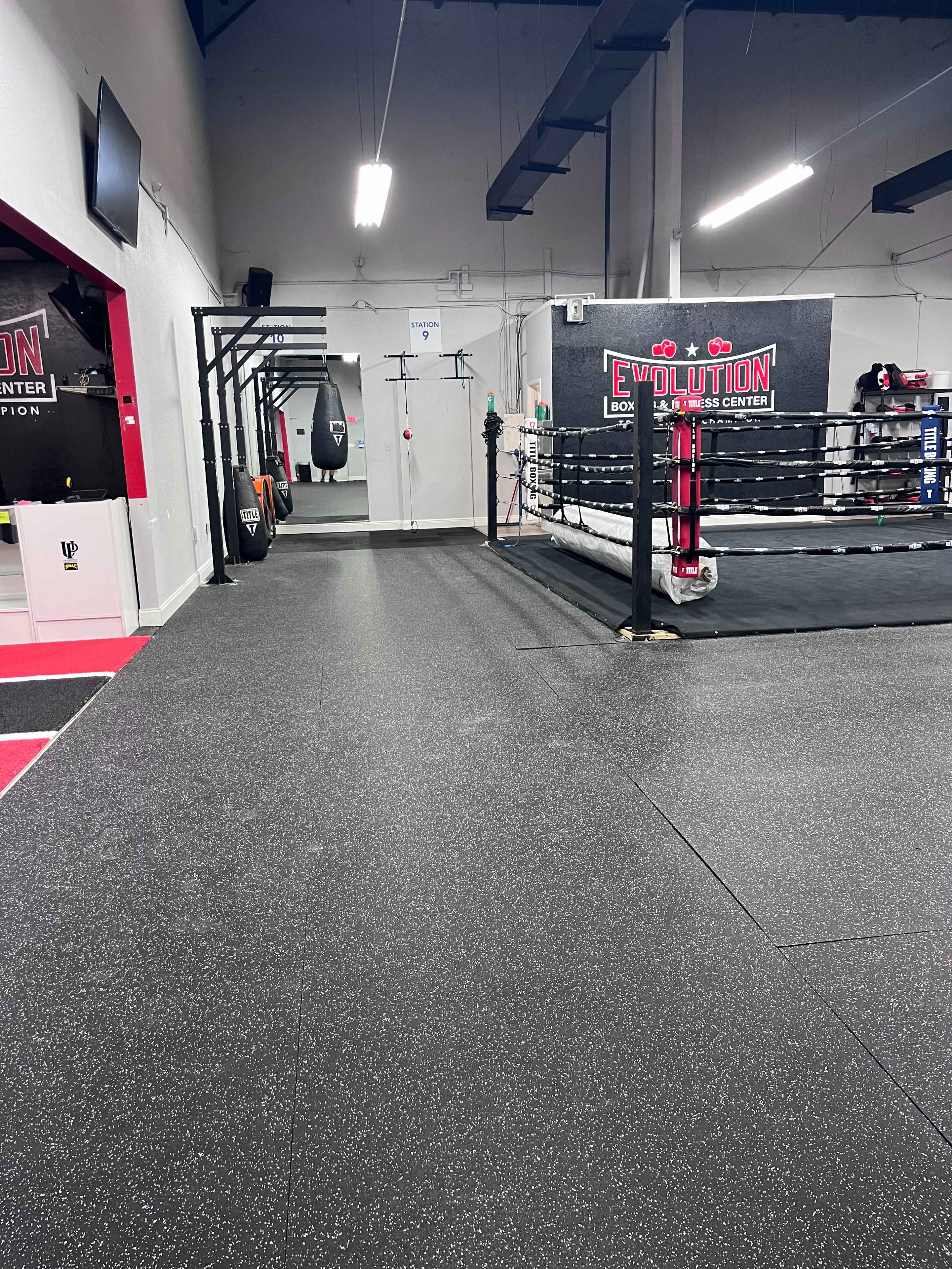 A gym interior featuring a boxing ring, punching bags, and rubber flooring.