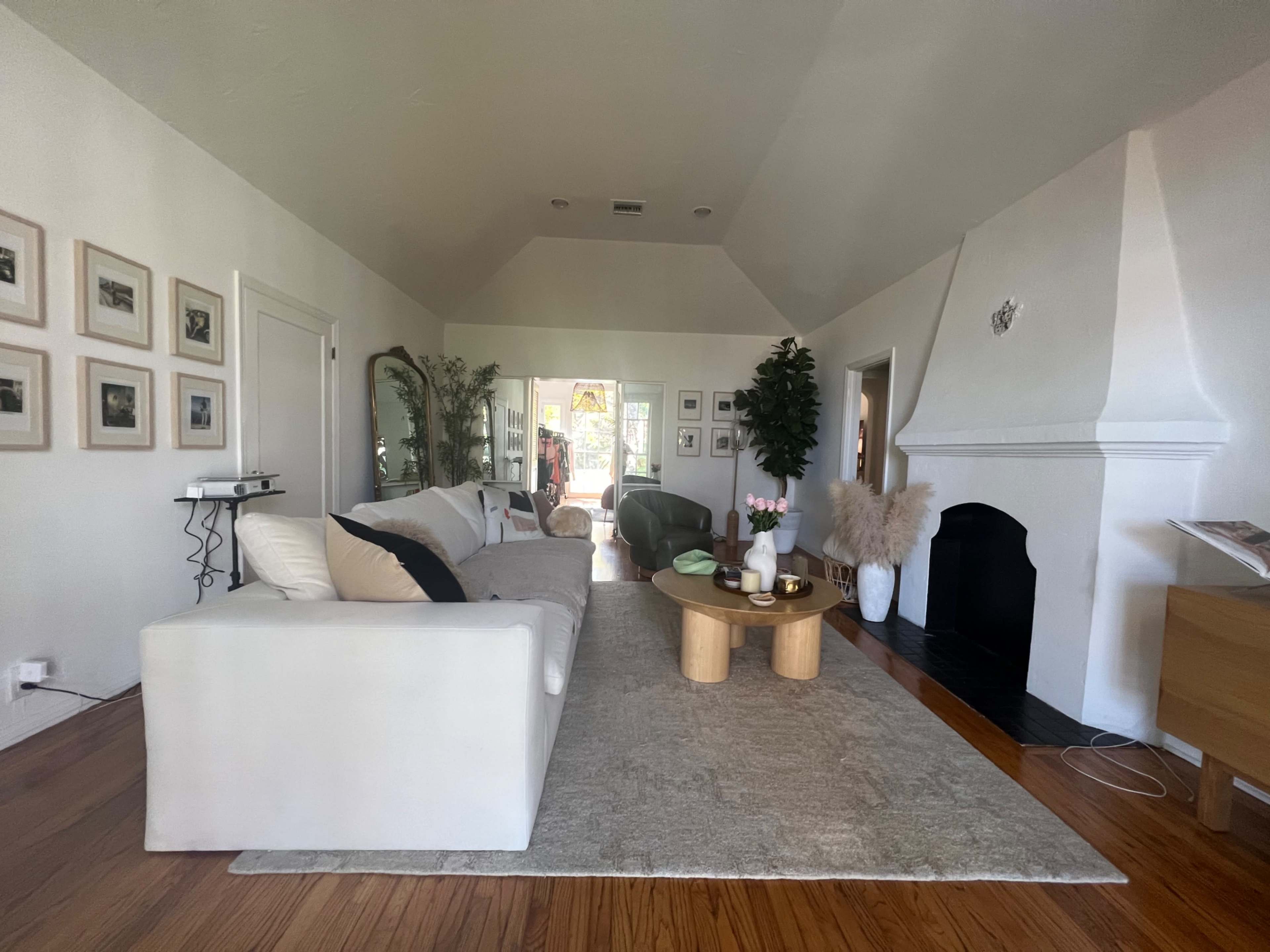 A bright living room with a white sofa, a wooden coffee table, and a large window leading to an outdoor area.