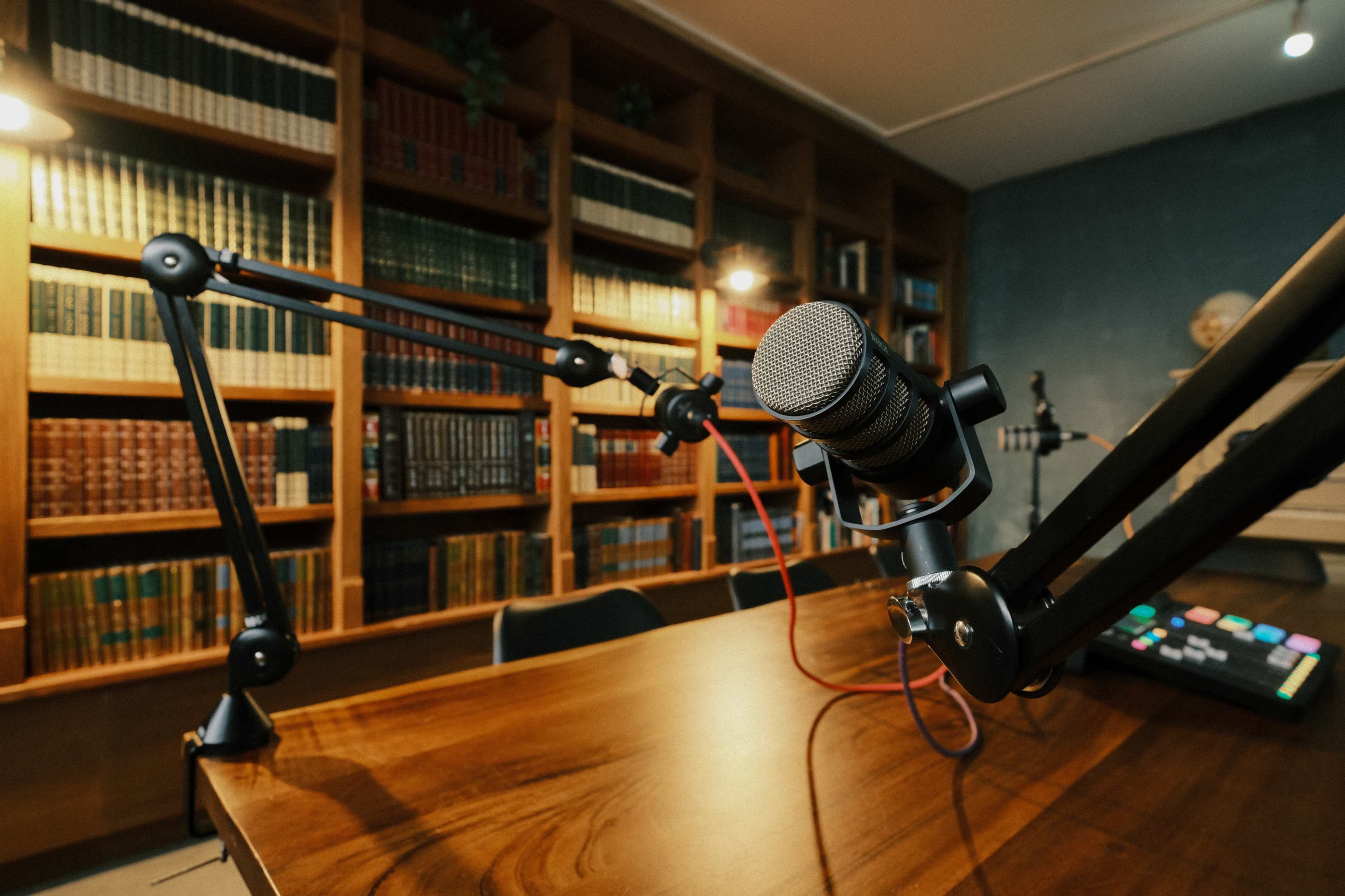 A microphone is positioned on a wooden desk in a room lined with bookshelves filled with books.