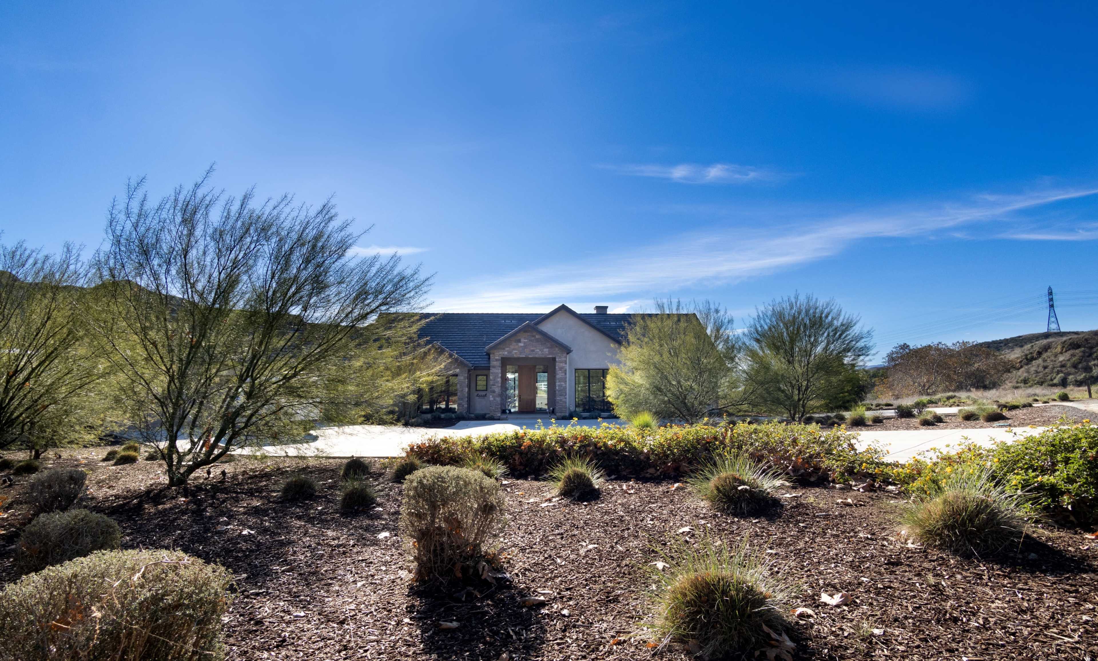 A modern house with a stone front entrance is surrounded by drought-resistant landscaping under a clear blue sky.