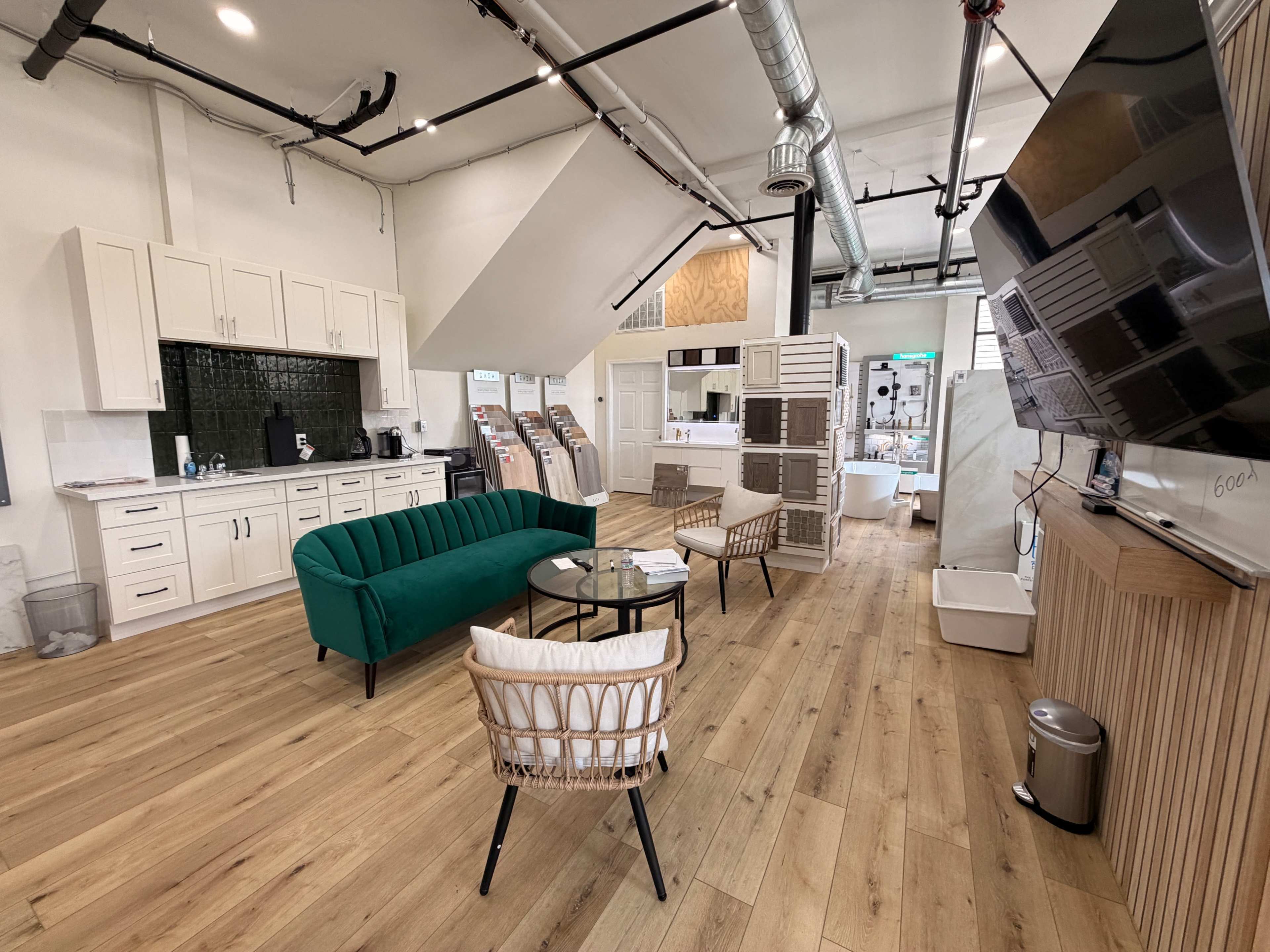 The image shows a modern communal workspace with a green couch, several chairs, a coffee station, and wooden flooring.