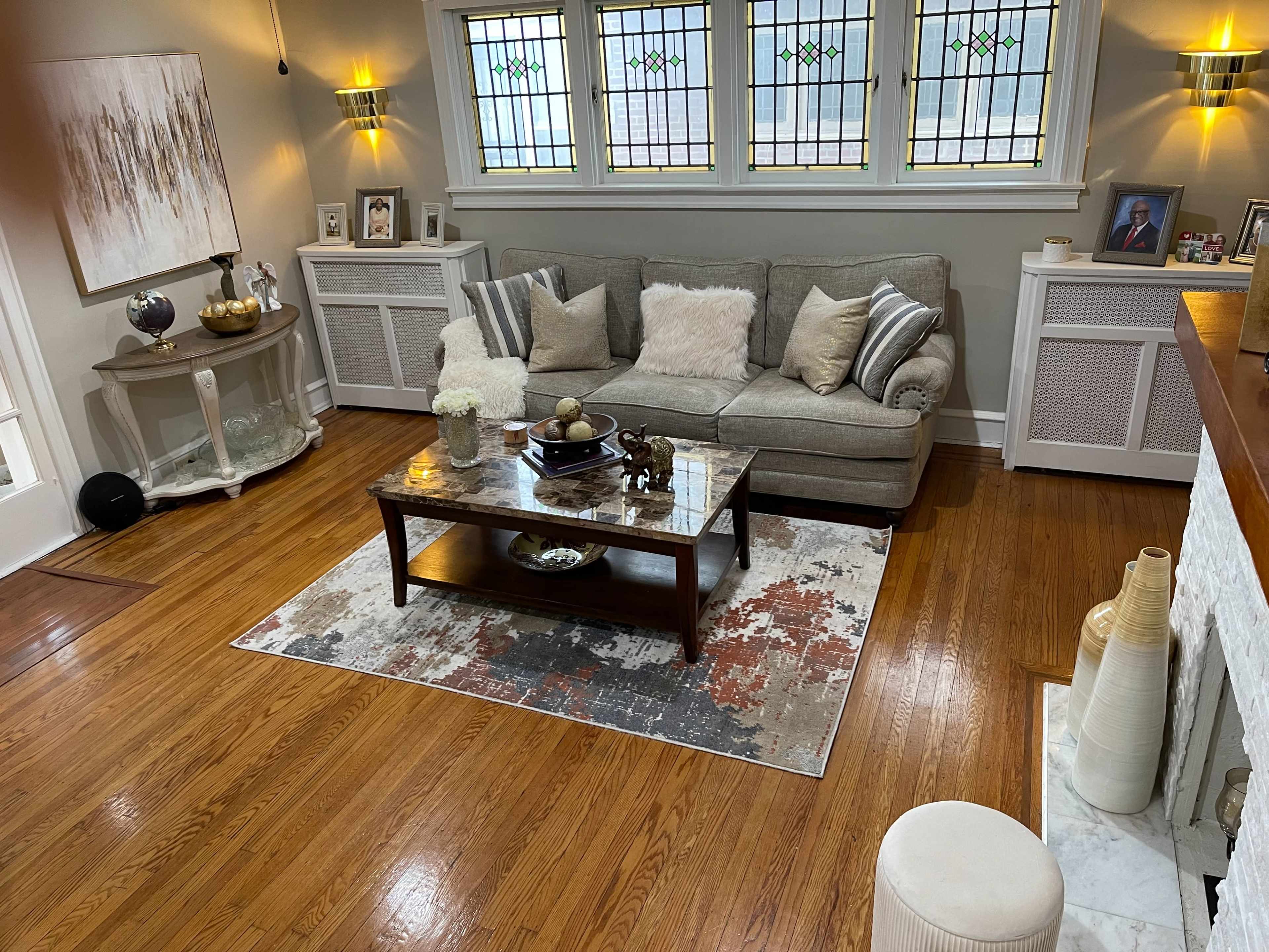 A cozy living room with a gray sofa, a wooden coffee table on a patterned area rug, and various decorative items on a side table and shelves.