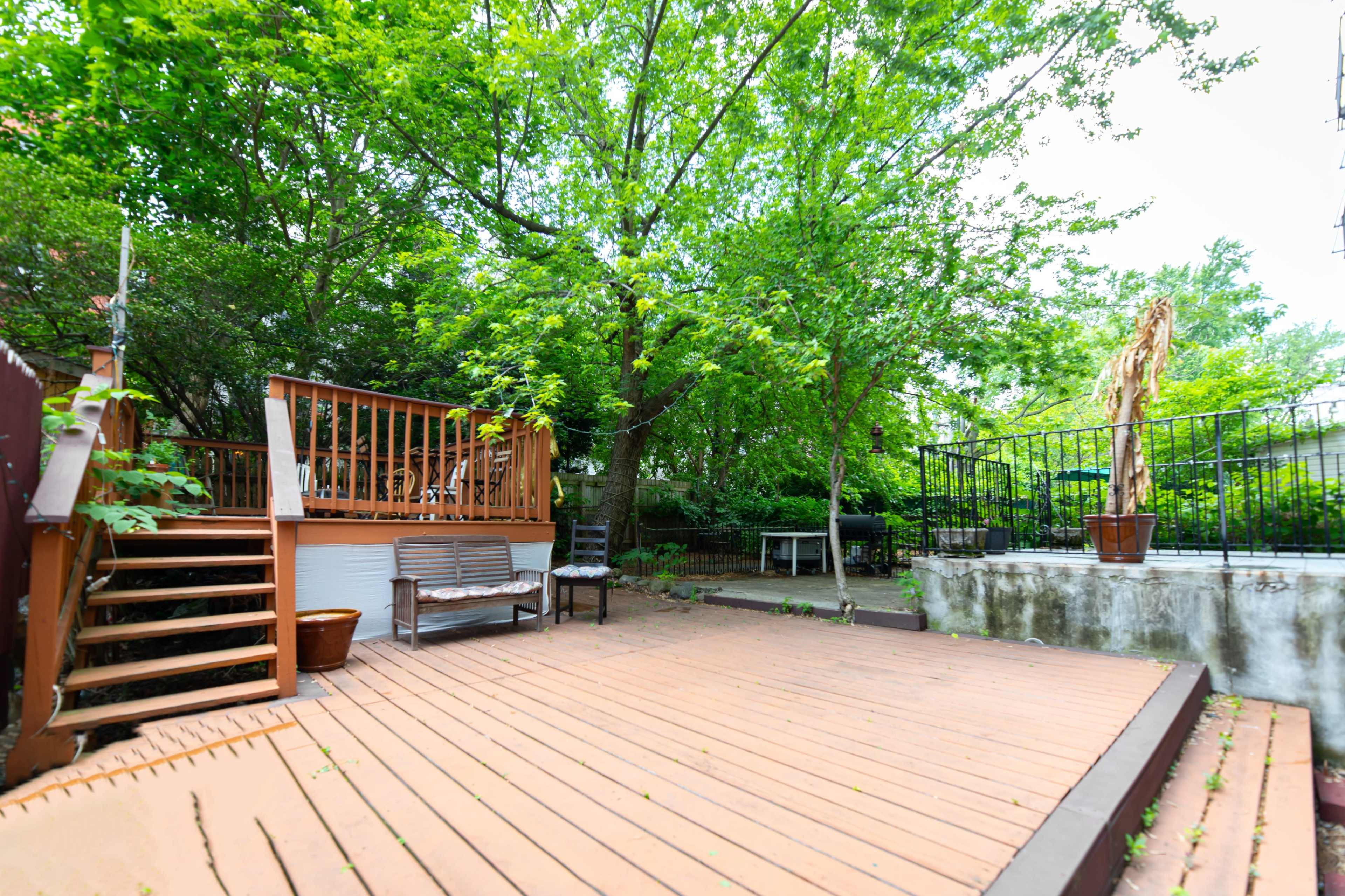 A wooden deck with seating overlooks a landscaped yard filled with trees and greenery.