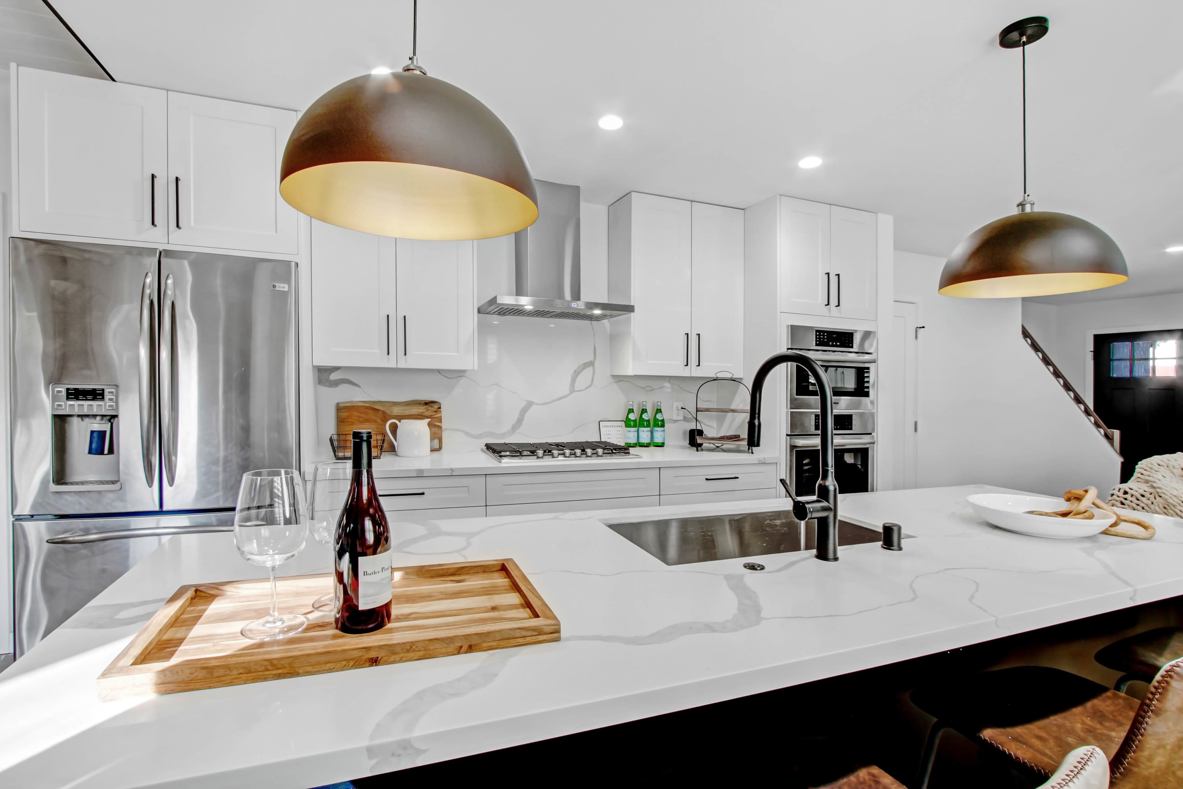 A modern kitchen features stainless steel appliances, white cabinetry, a marble countertop, and pendant lights over the island.