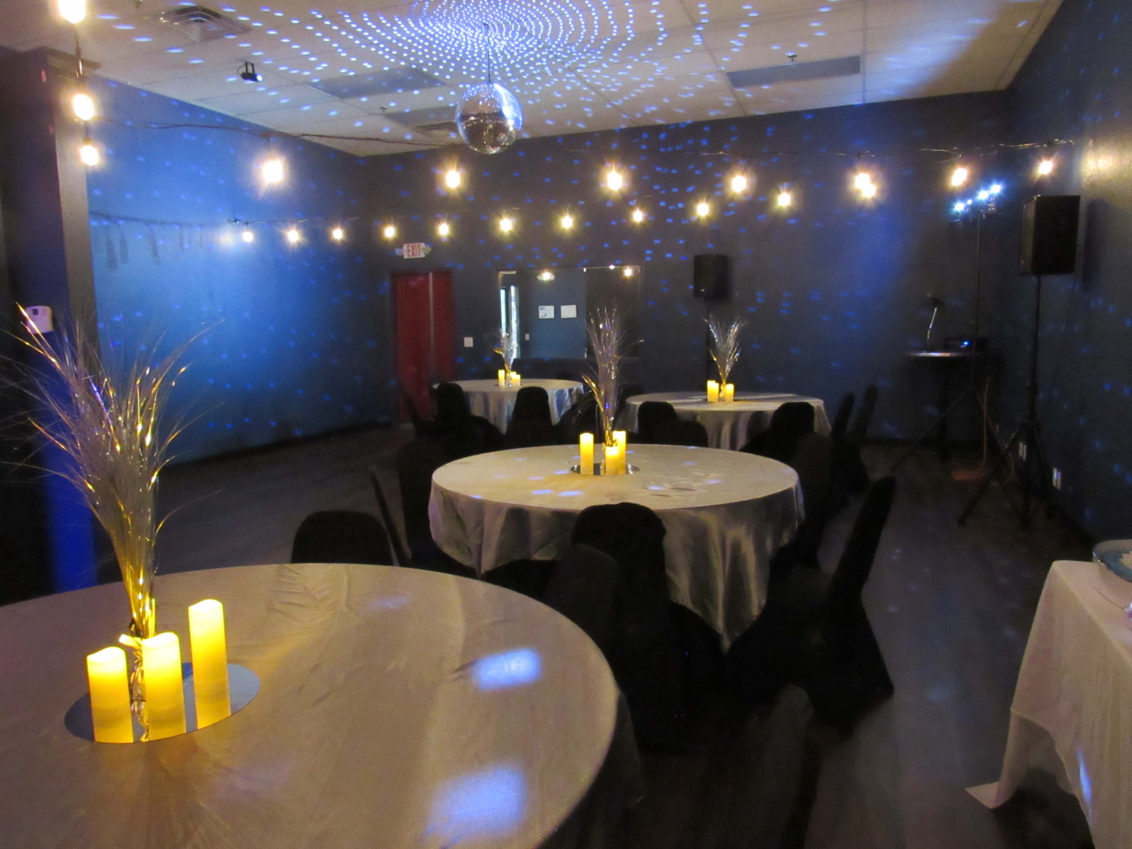 The image shows a dimly lit event space with round tables decorated with candles and illuminated by a disco ball casting light patterns on the walls.