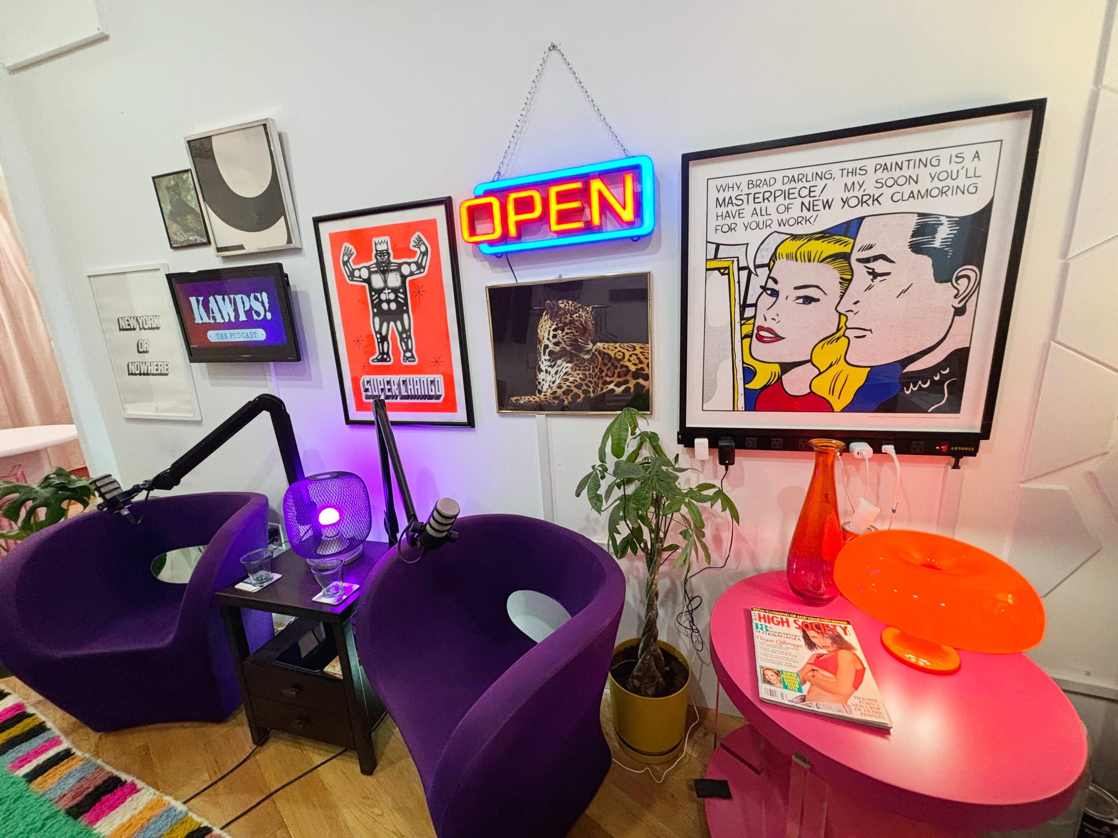 The image shows a vibrant room with two purple chairs, colorful artwork on the walls, and a neon "OPEN" sign.