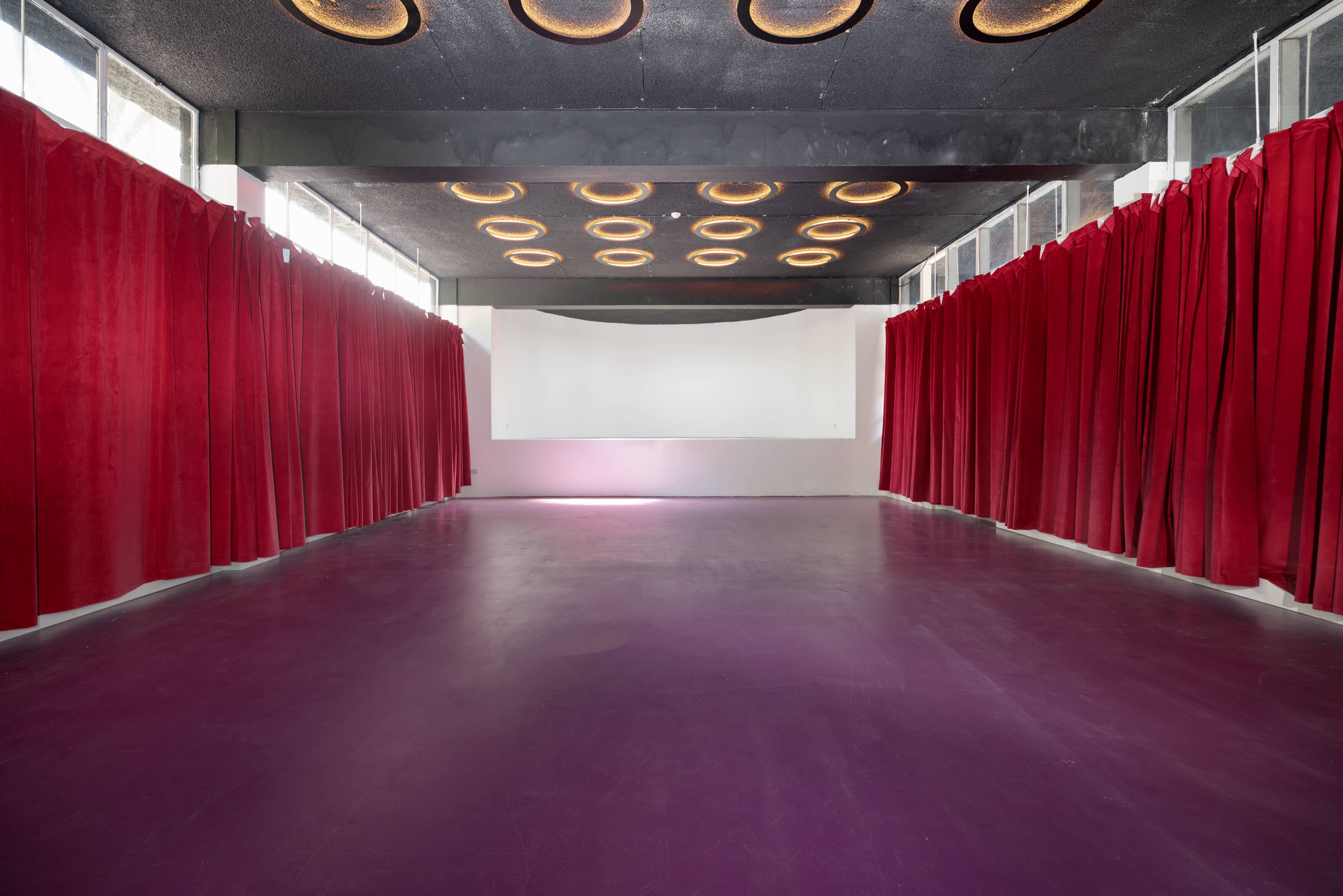 The image shows a spacious room with red velvet curtains lining the walls and a white projection screen at the far end.