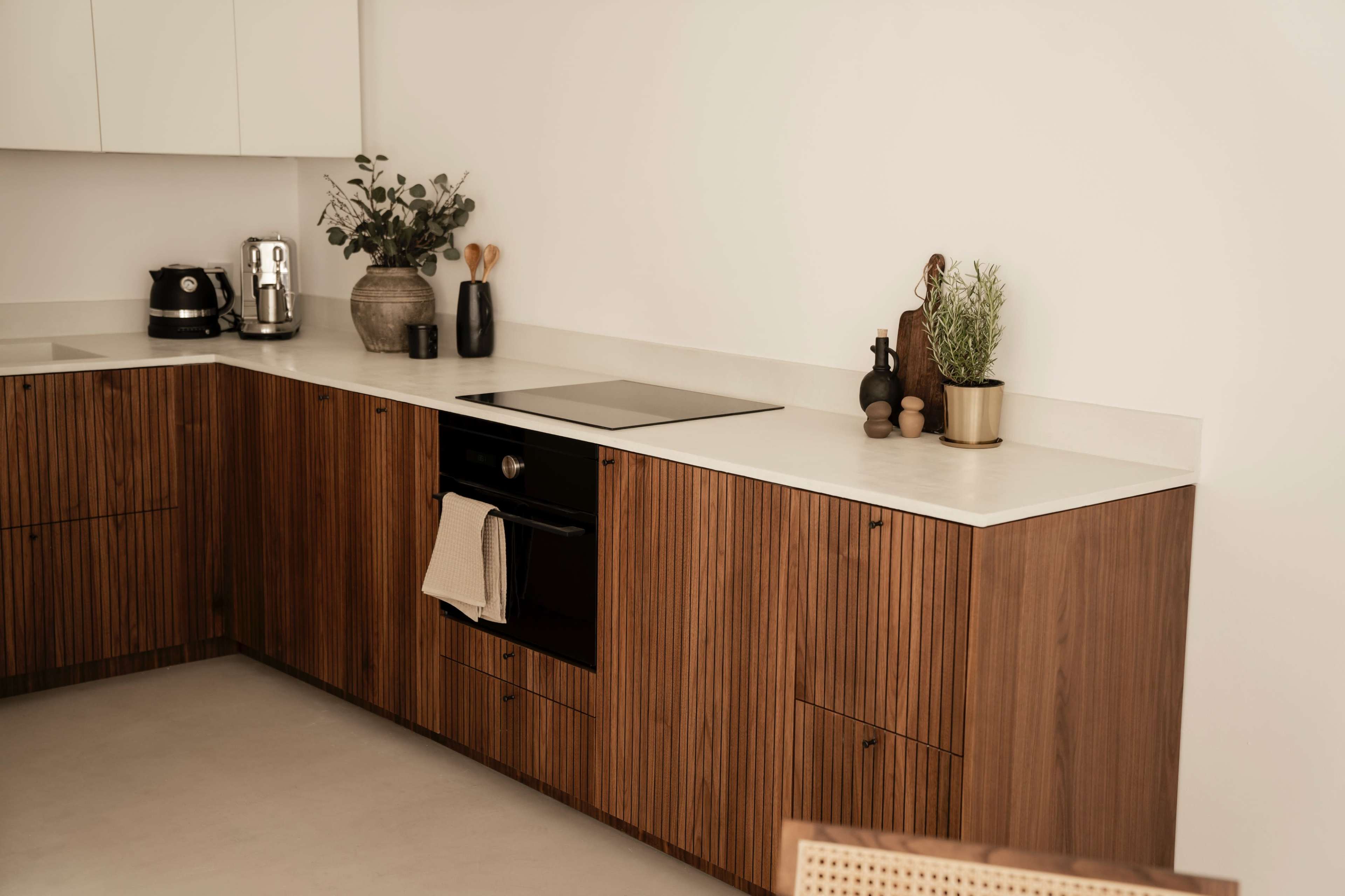 A modern kitchen features a minimalist design with wood cabinetry, a black oven, and a few decorative plants on the counter.