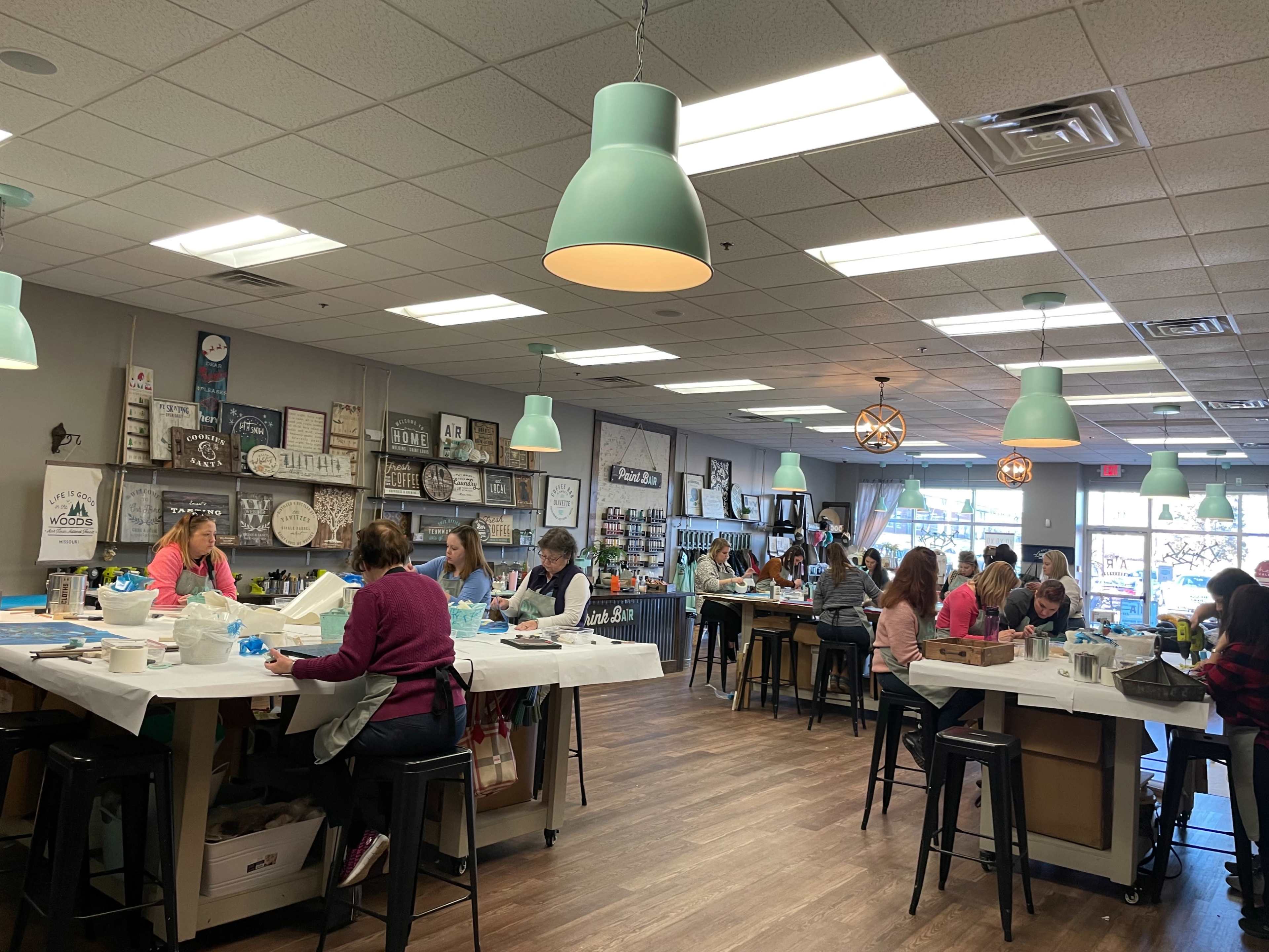 A spacious art studio filled with people engaged in various crafting activities at long tables.